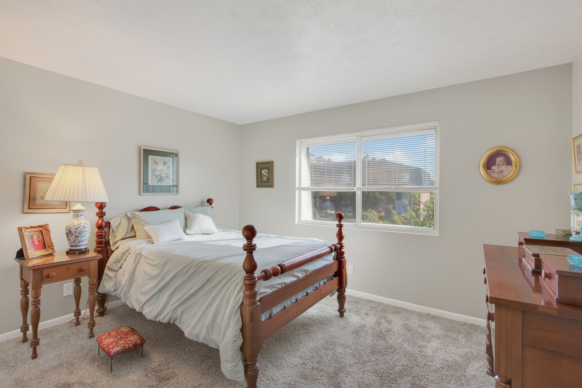 Bright bedroom with wooden bed, beige walls, window, and carpeted floor
