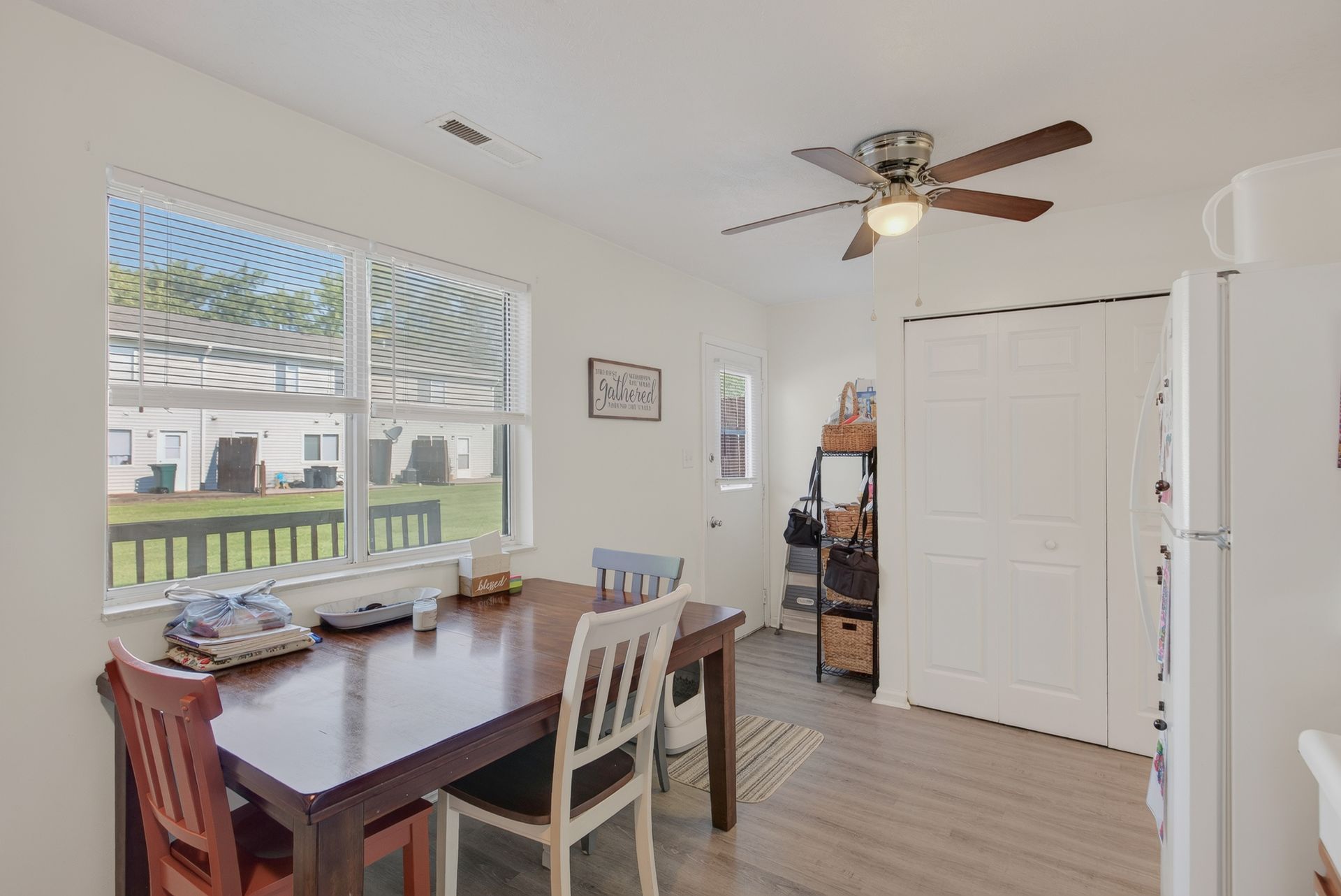 Bright kitchen nook with dining table, window, ceiling fan, and white cabinets overlooking a backyard
