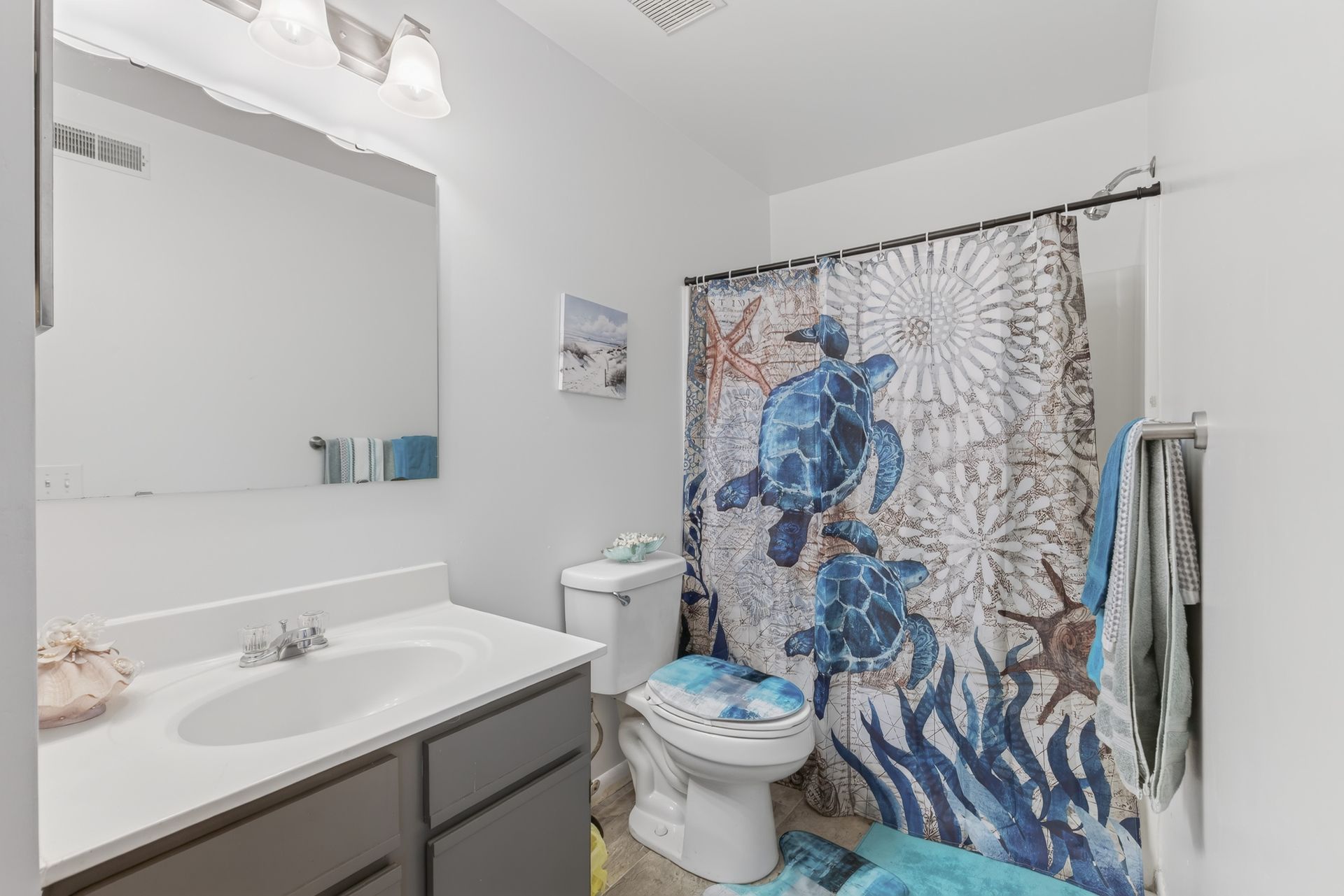 Small bathroom with a white sink, toilet, and blue ocean-themed shower curtain.