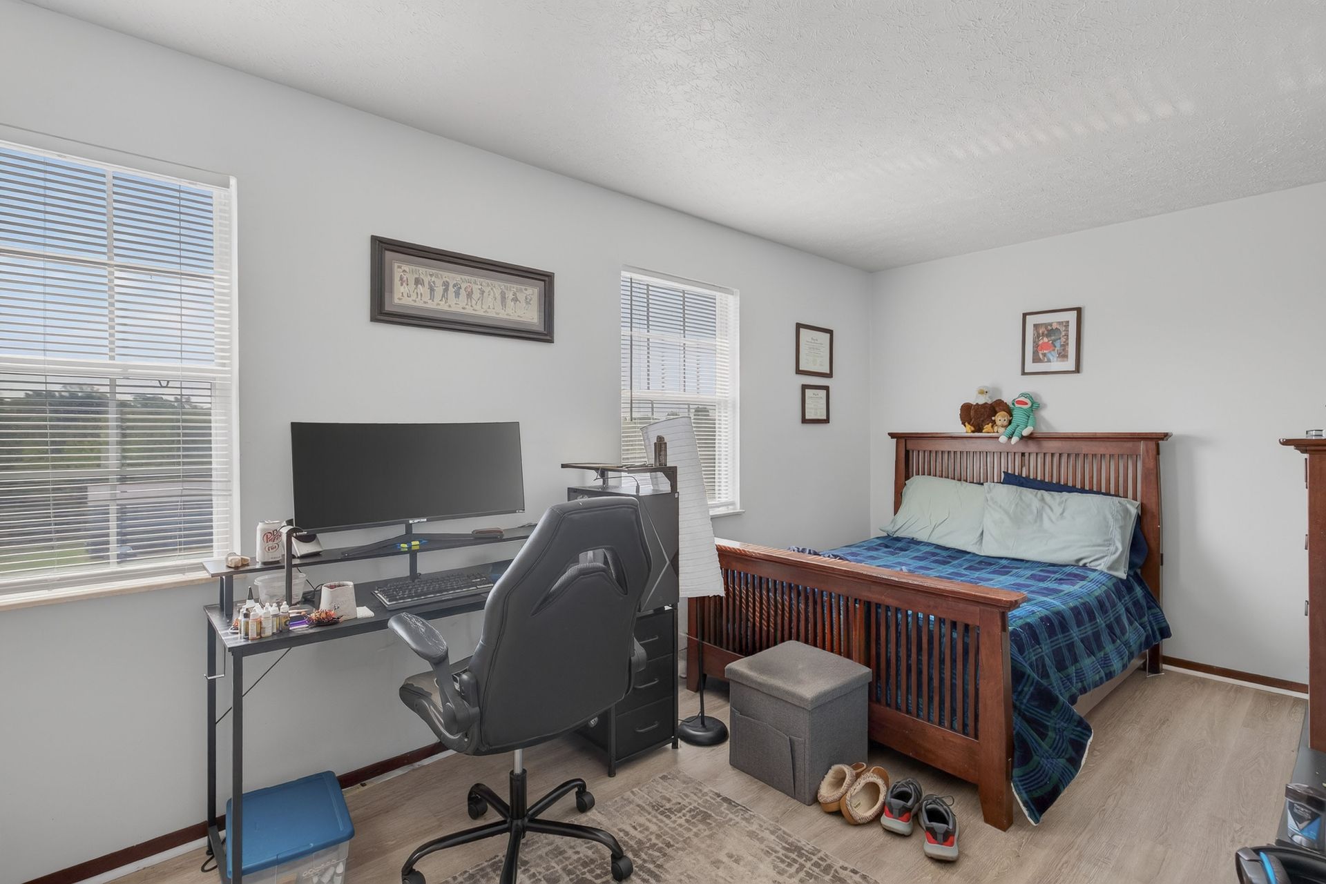 Small bedroom office with desk, computer, chair, and a wooden bed with blue bedding.