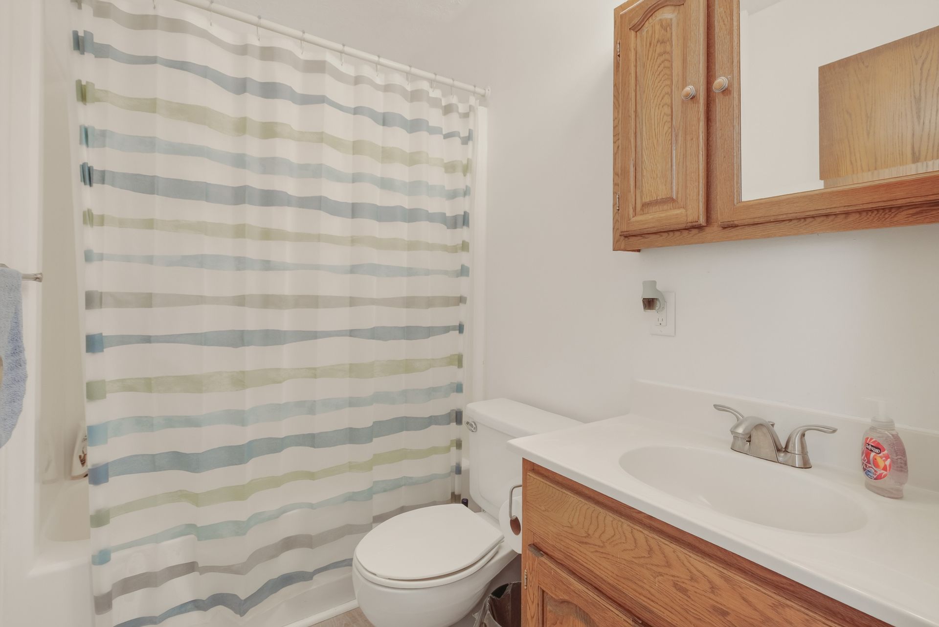 Small bathroom with striped shower curtain, toilet, and wooden vanity with sink and mirror.