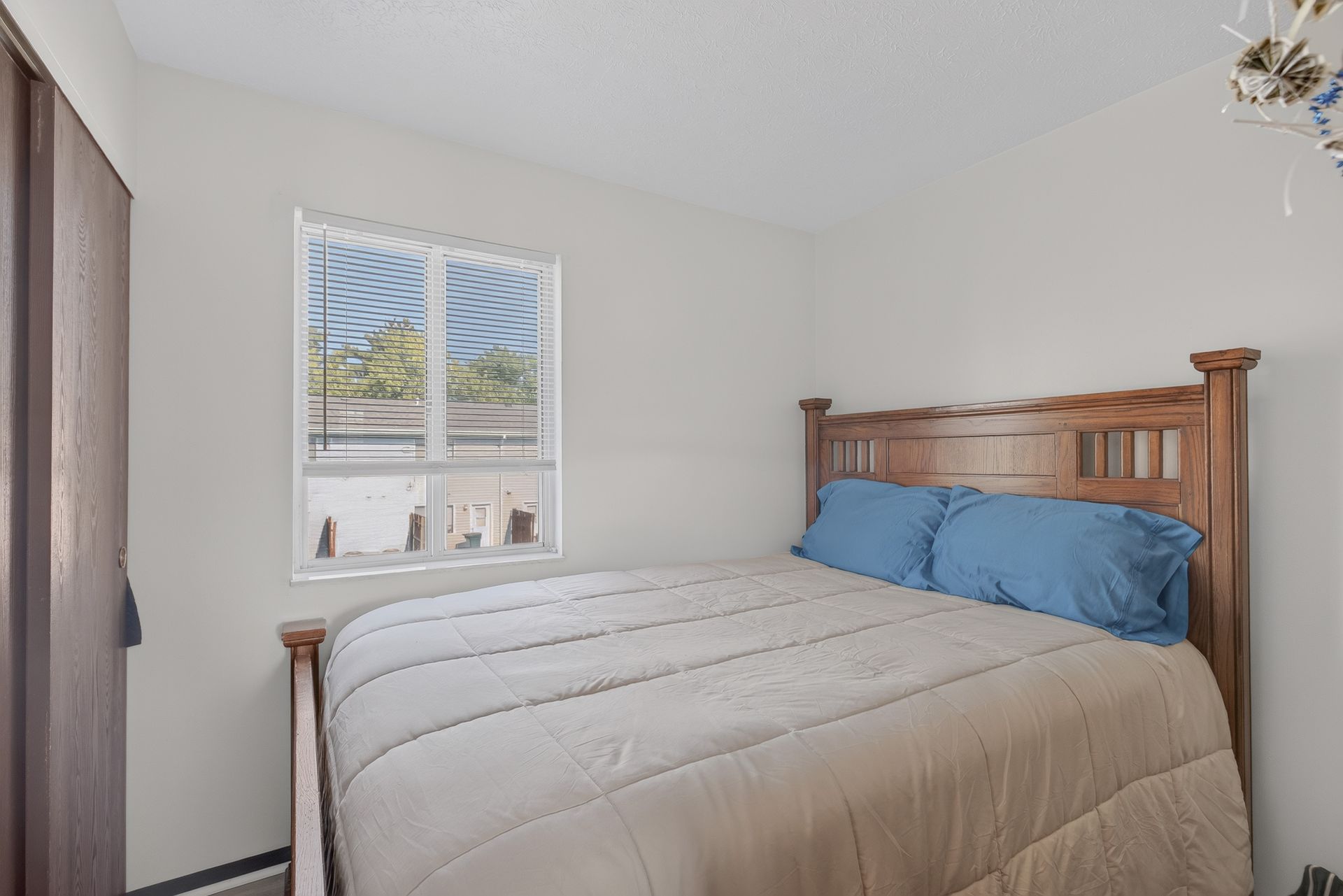 Small bedroom with a wooden bed, blue pillows, white bedding, and a window letting in daylight.