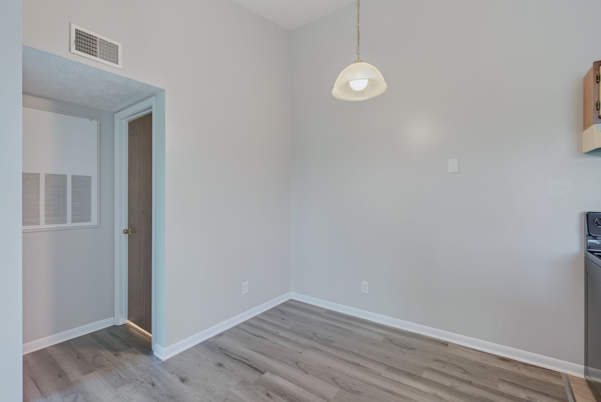 Empty gray room with wood flooring, a hanging light, and an open doorway to a hall