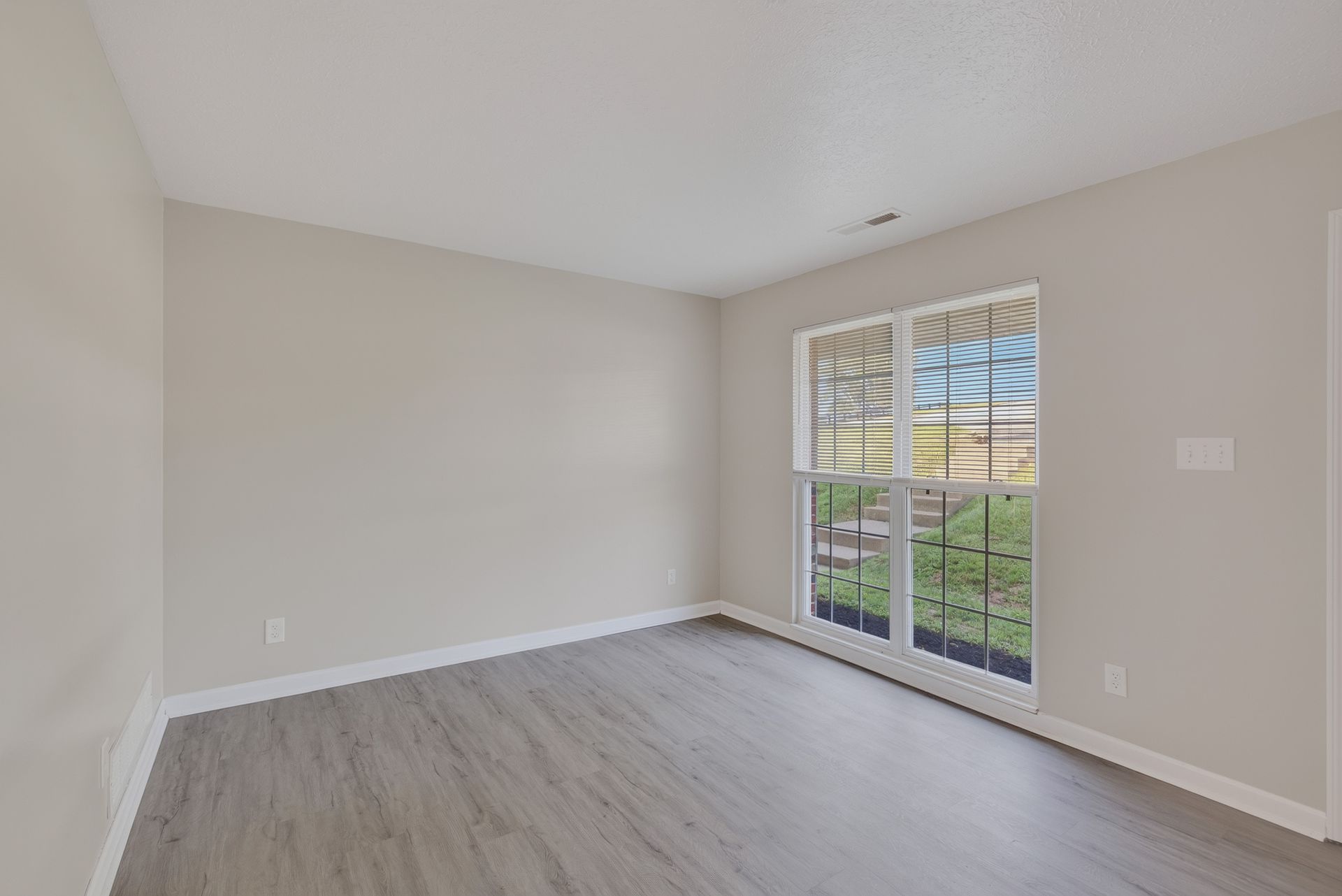 Empty beige room with light wood floors and a sliding glass door to a grassy yard