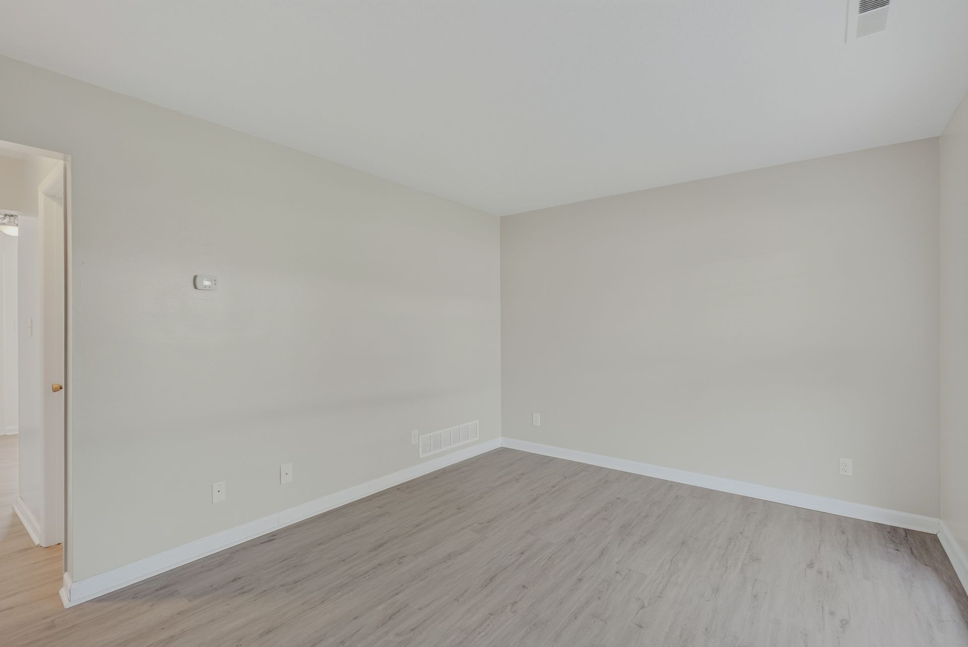 Empty beige bedroom with light wood flooring and white trim.