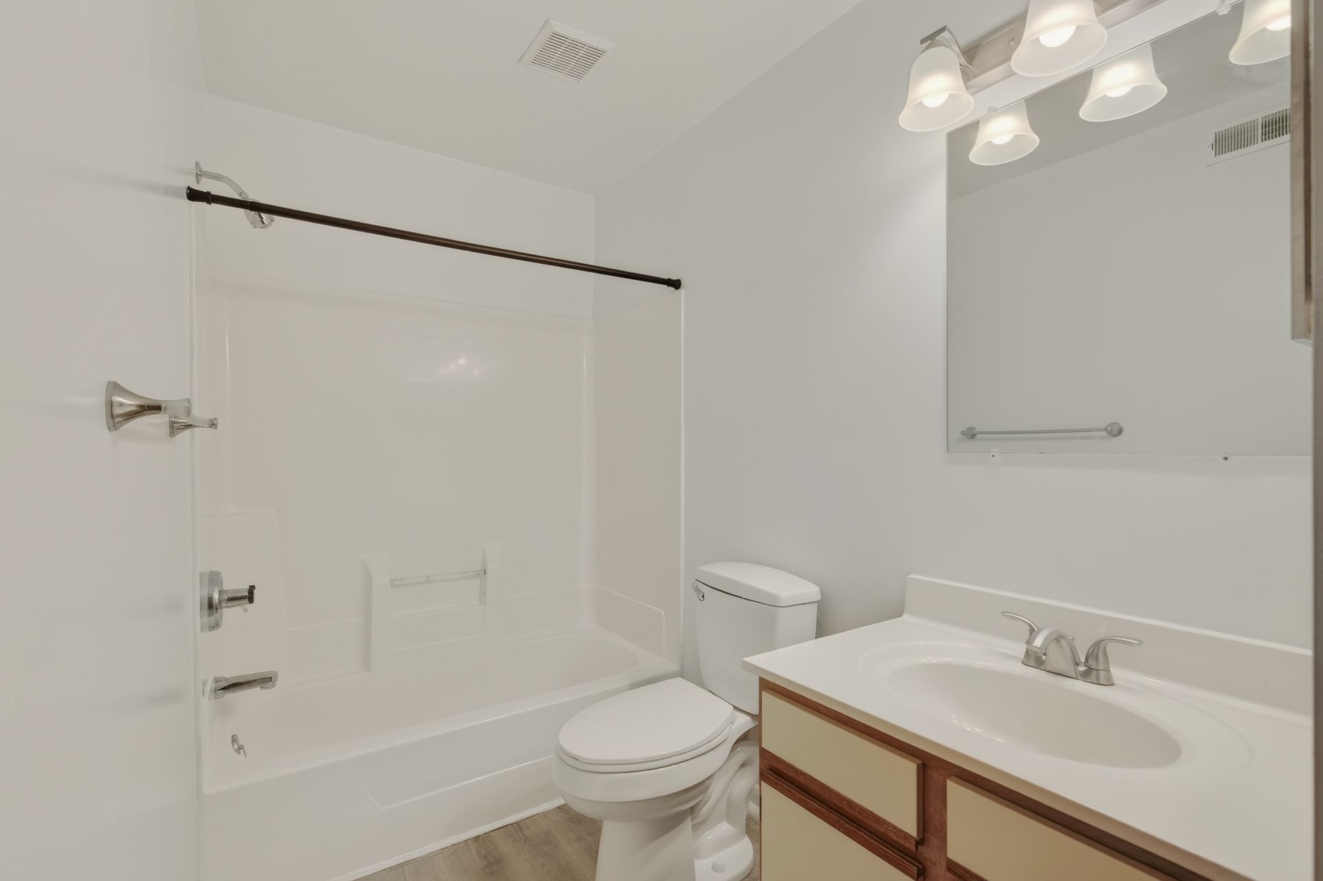 Bright white bathroom with tub-shower, toilet, and vanity sink under a large mirror.