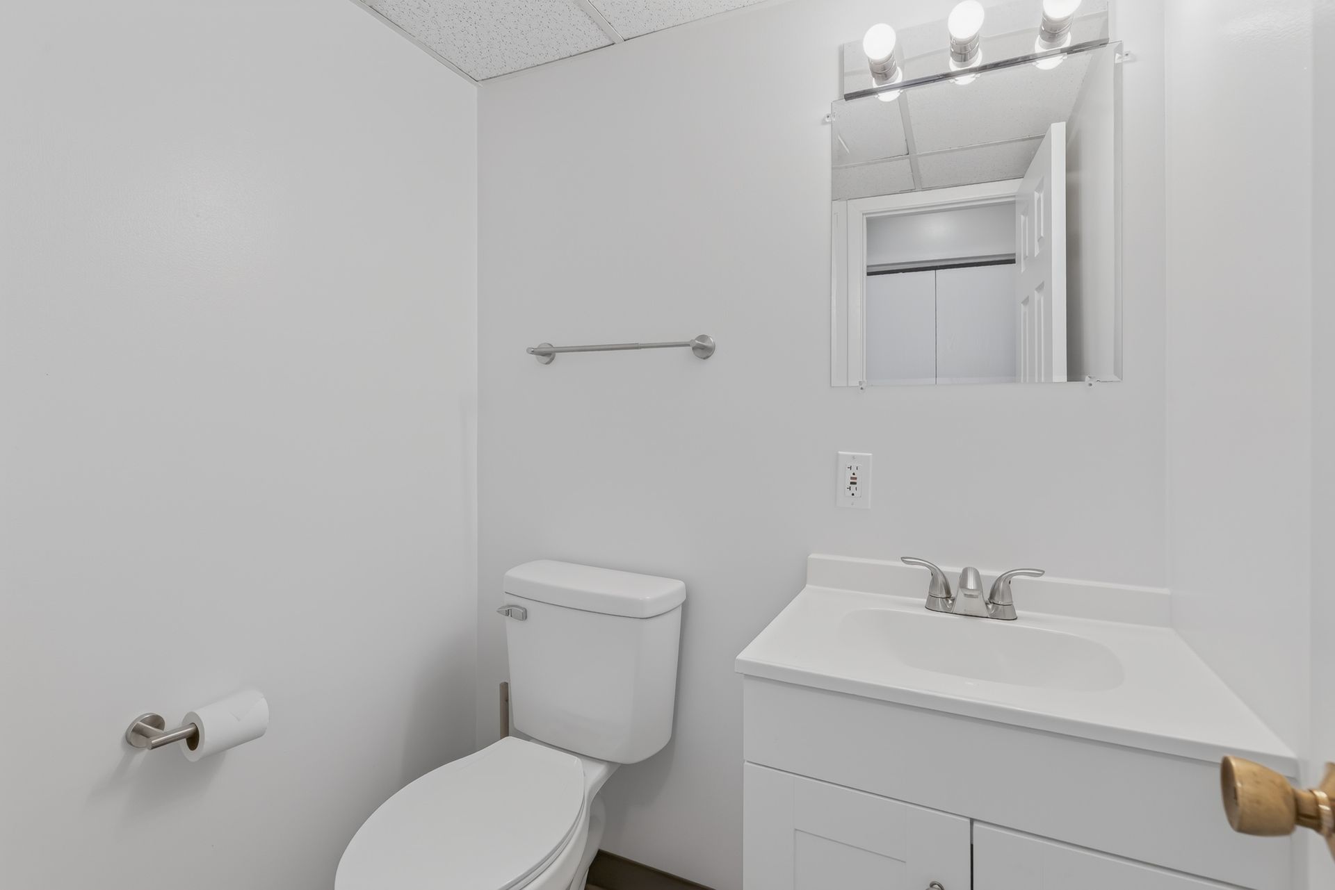 Small white bathroom with toilet, vanity sink, mirror, and towel bar.