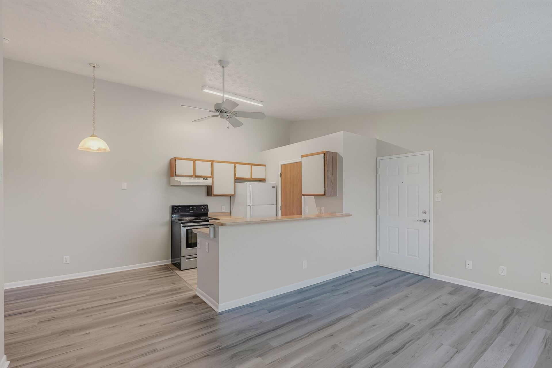 Empty modern kitchen and dining area with gray floors, white walls, and a hanging pendant light.