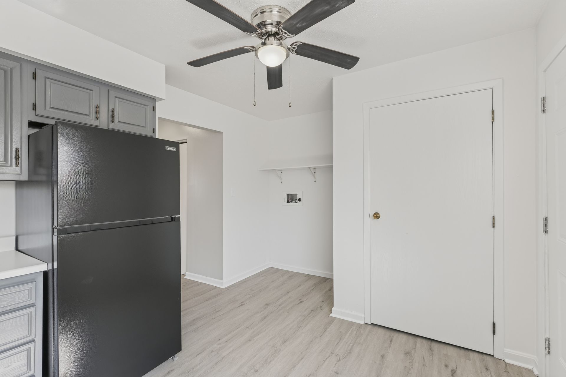 Bright empty kitchen with black refrigerator, gray cabinets, ceiling fan, and white walls
