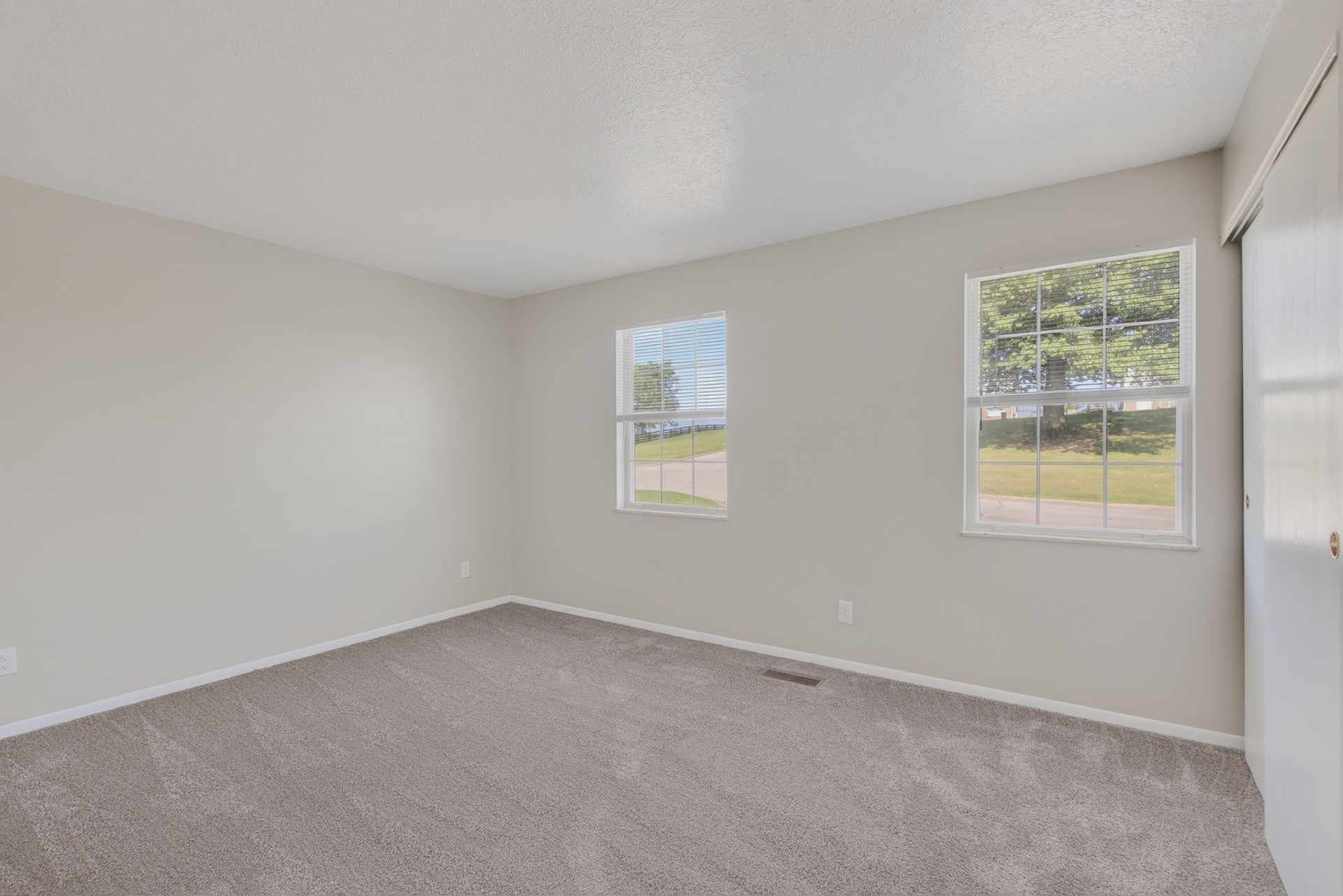 Empty carpeted bedroom with light gray walls and two windows