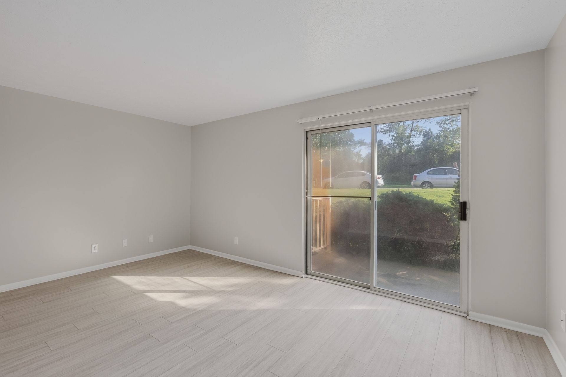 Empty light-gray room with sliding glass door and sunlight on the floor