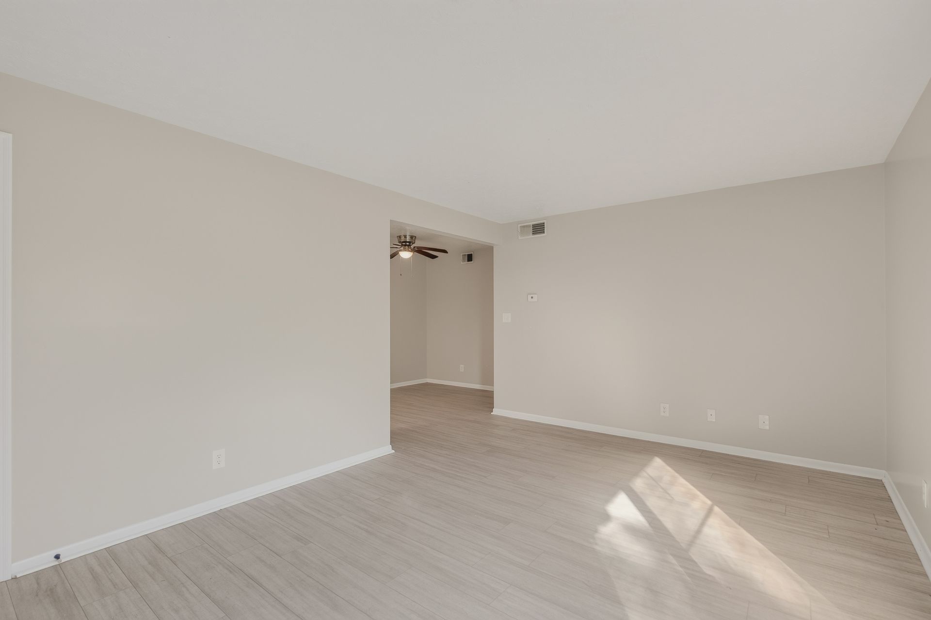 Empty beige living room with light wood floors and sunlight on the wall