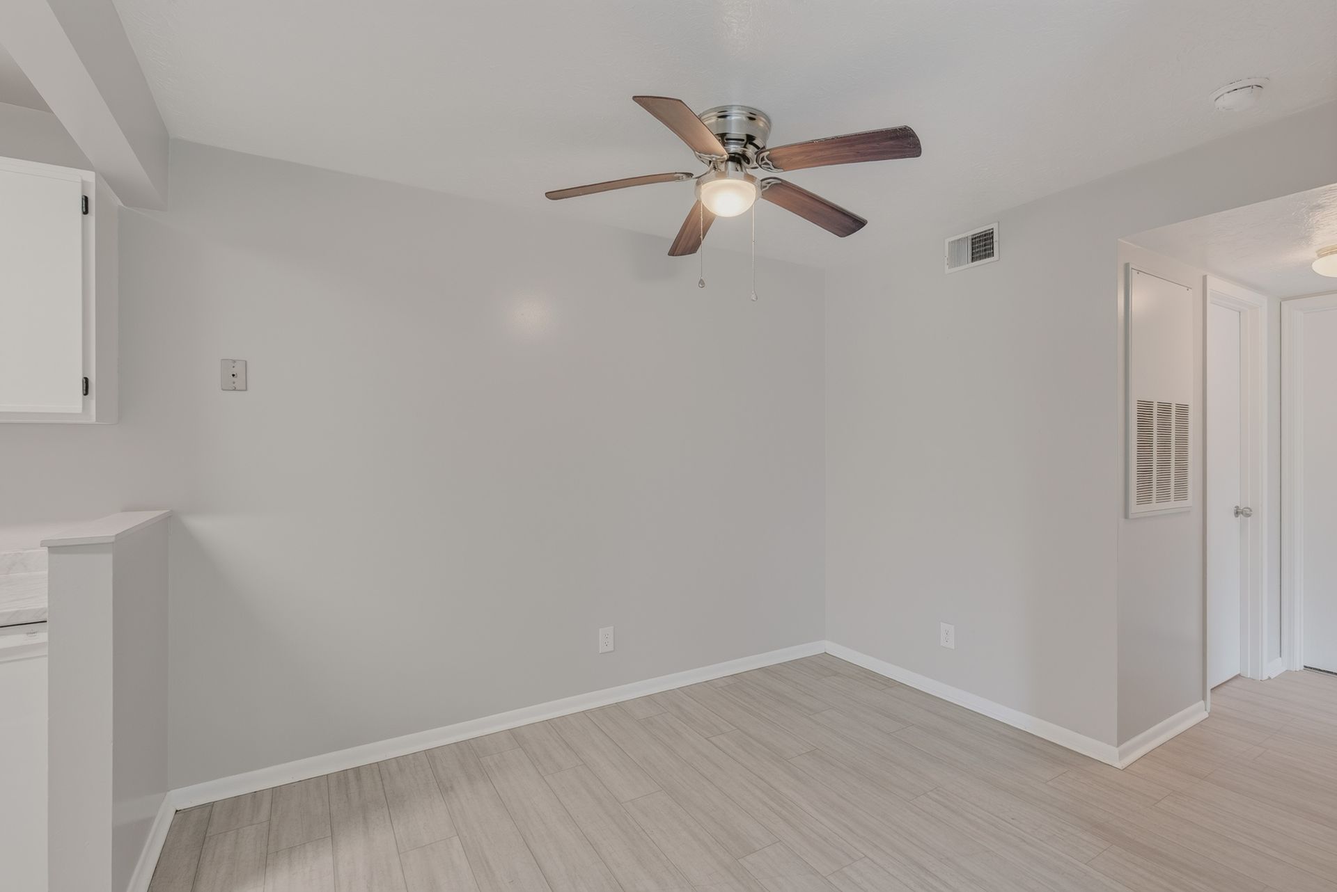 Empty light gray bedroom with a ceiling fan and wood-look flooring