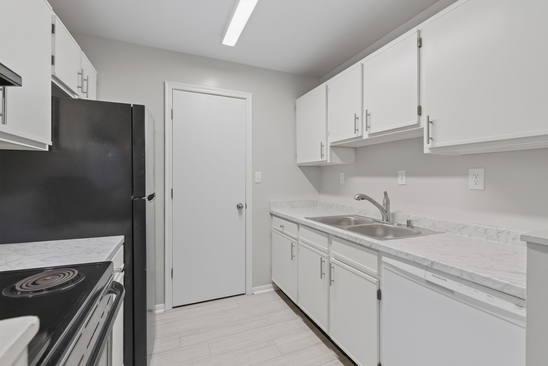 Bright white kitchen with black appliances, white cabinets, and a sink along the right wall