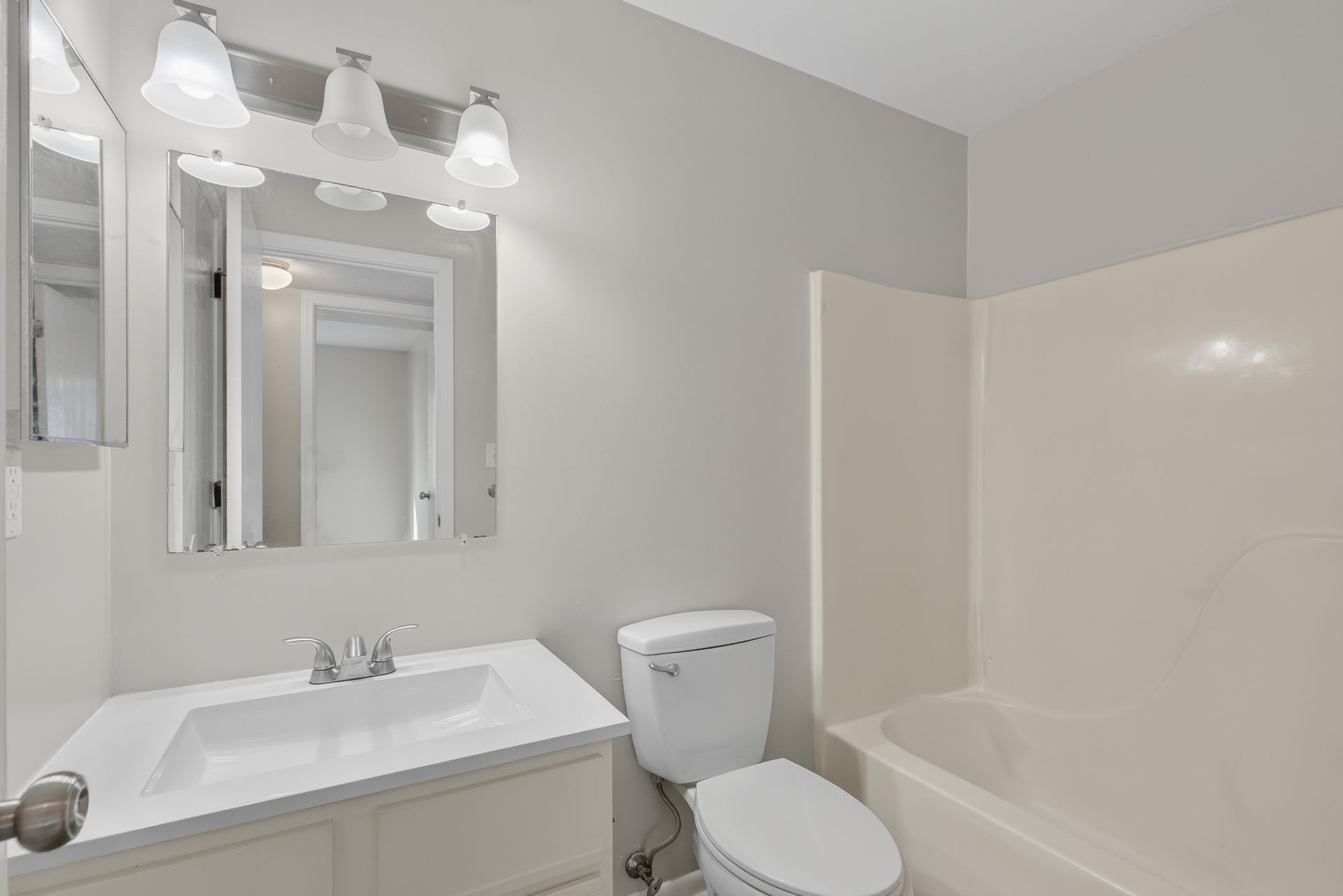 Bright bathroom with white sink, mirror, vanity lights, toilet, and bathtub.