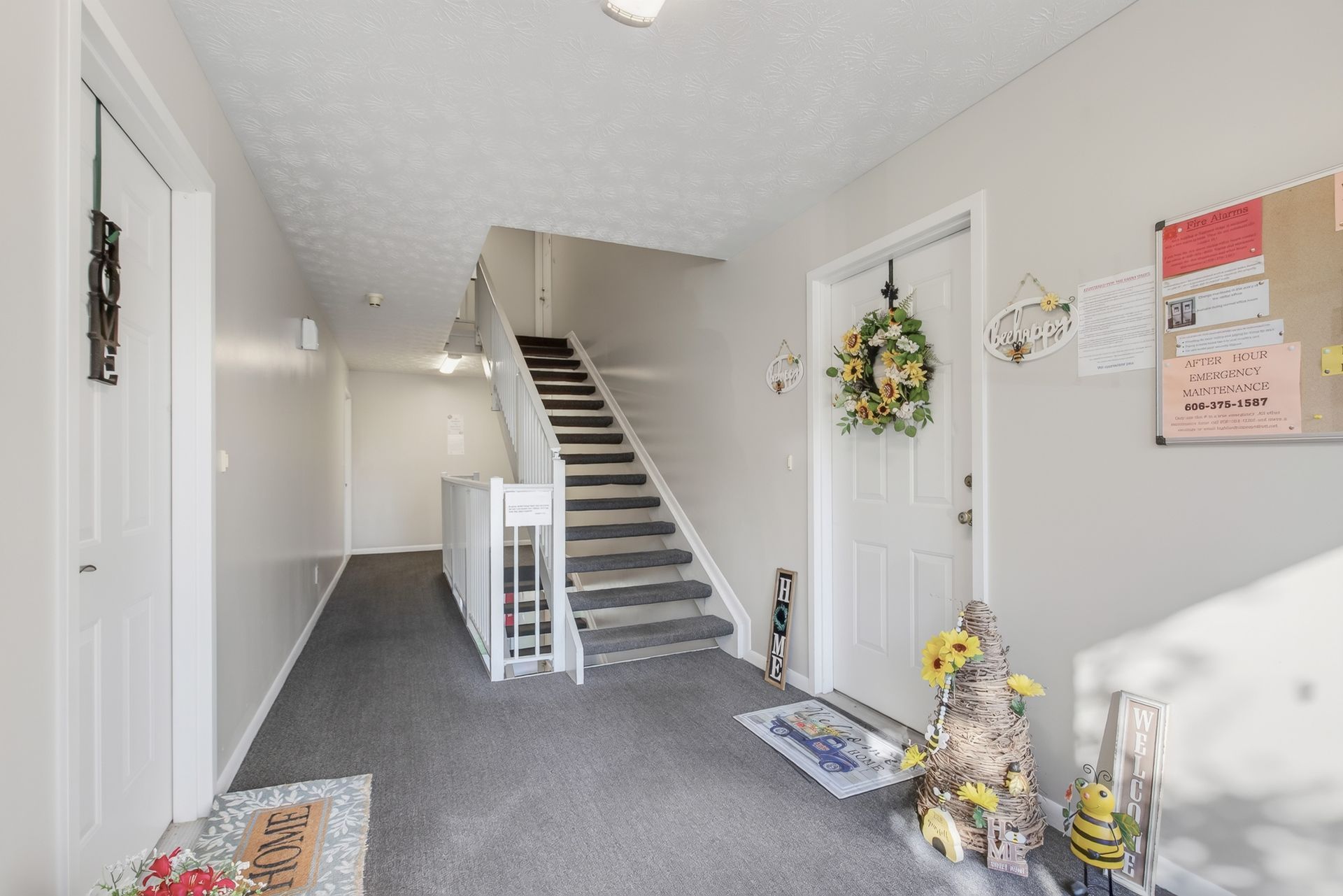 Bright hallway with carpeted staircase, white walls, and a front door decorated with a wreath.