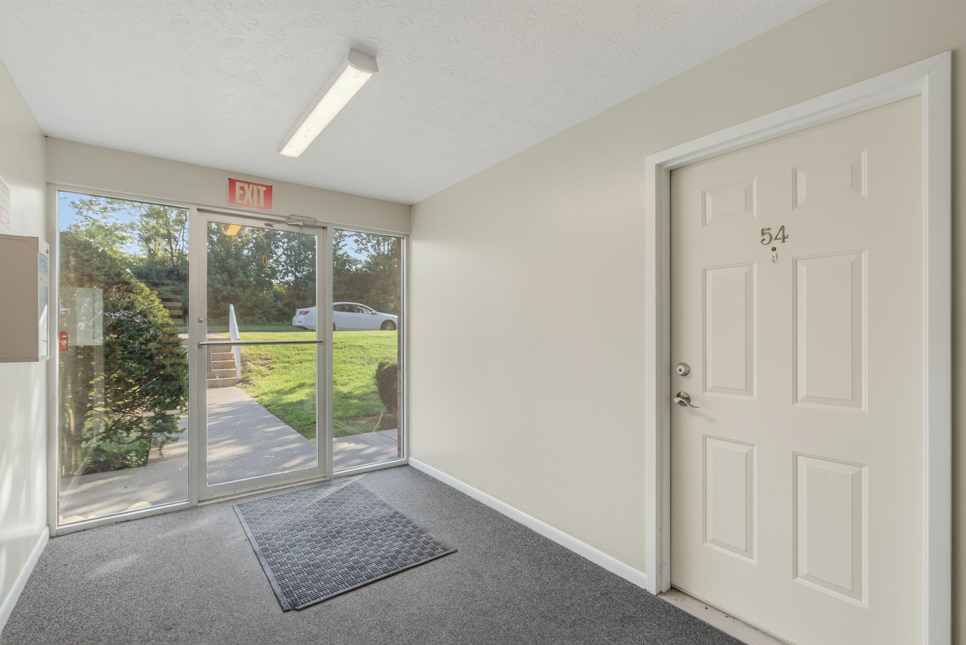 Small entryway with glass front door, white walls, carpeted floor, and a side door.