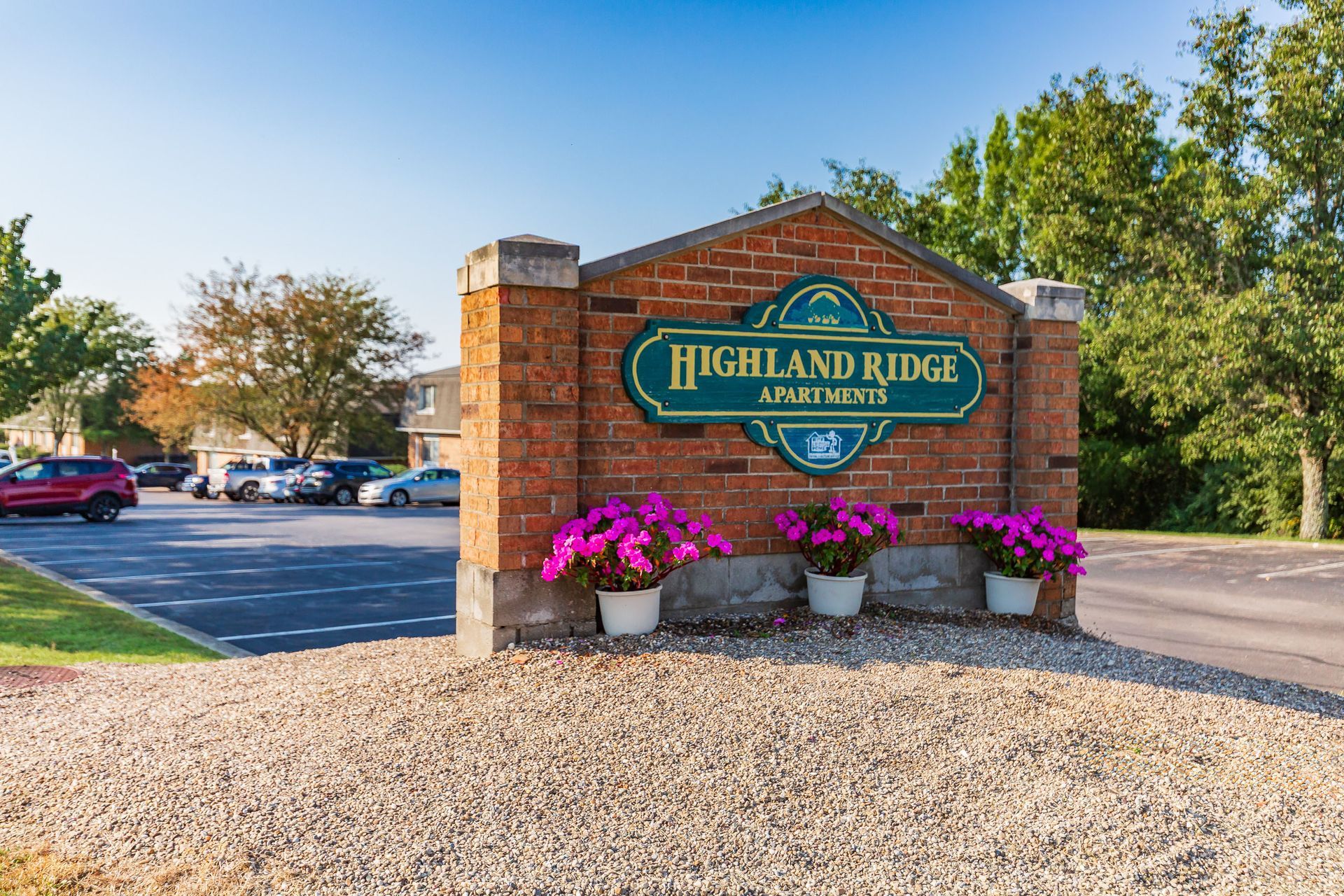 Highland Ridge Apartments sign with pink flowers beside a parking lot on a sunny day