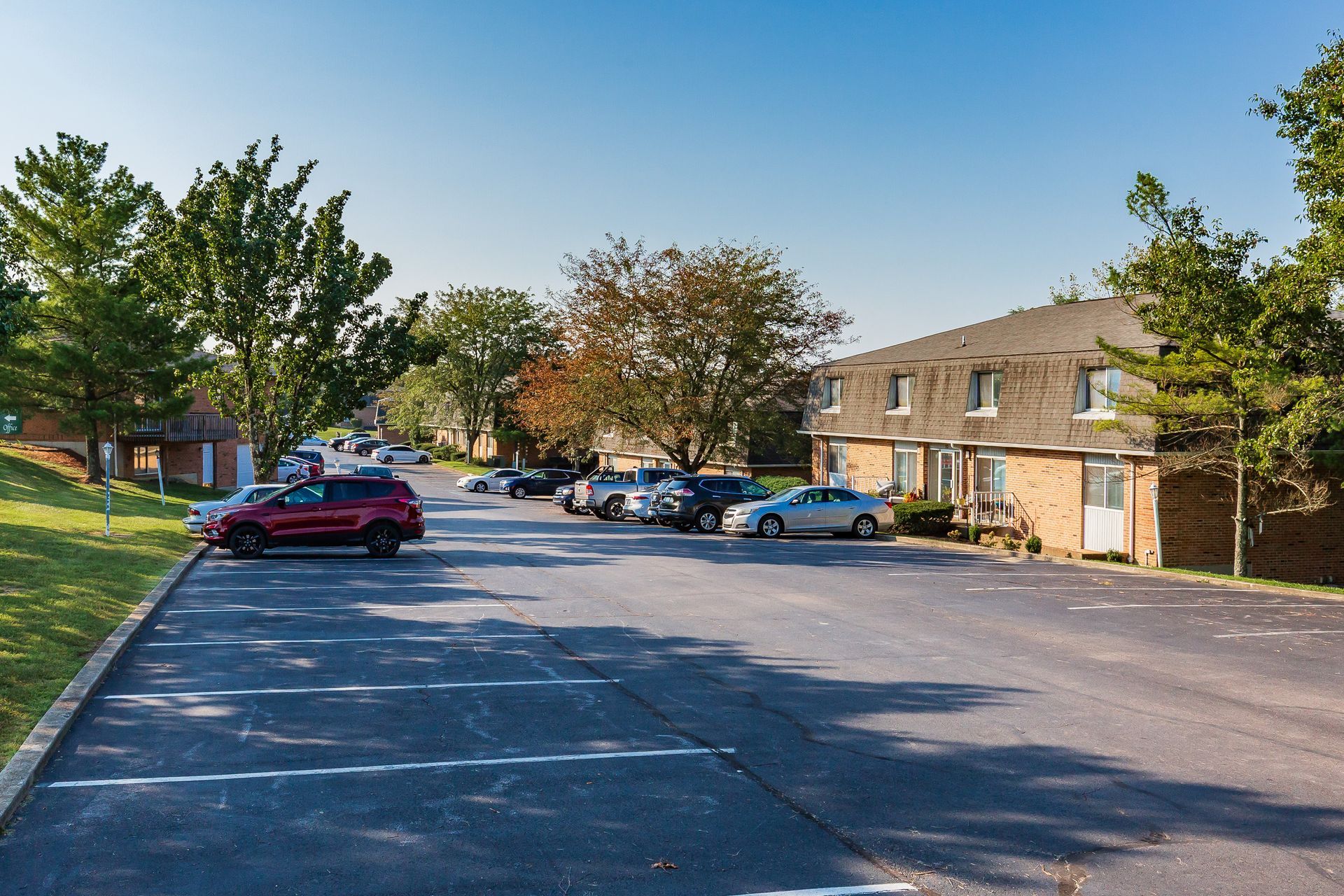 Suburban apartment parking lot with cars, brick buildings, and trees on a sunny day