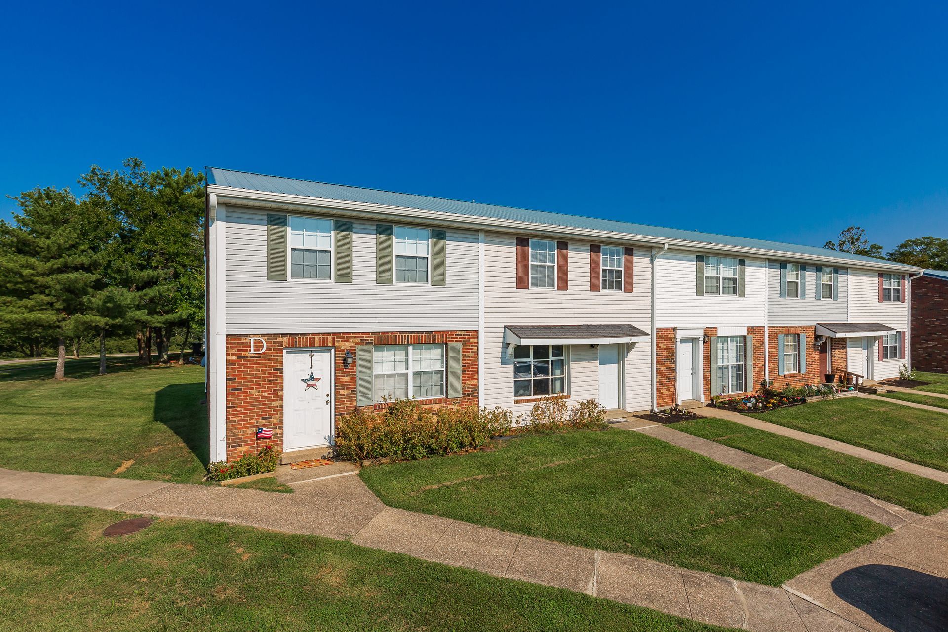 Row of white and brick townhouses with green lawns under a clear blue sky