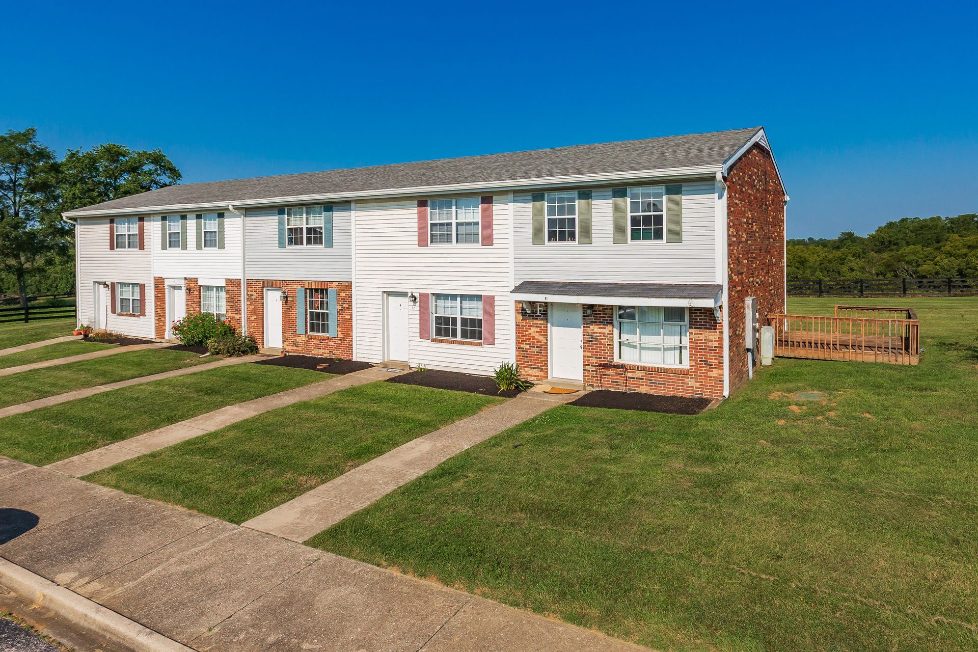 Row of white brick townhouses with red accents, front lawns, and a blue sky