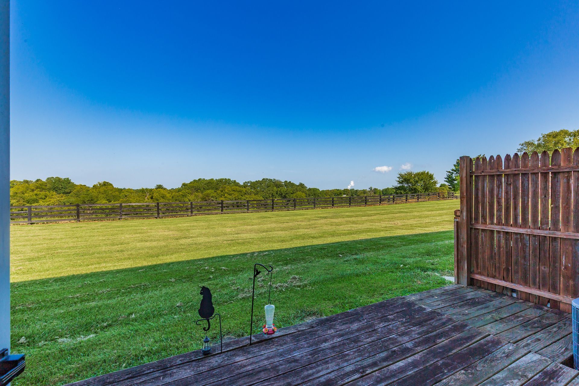 Wooden deck overlooking a grassy backyard with a fence and blue sky.