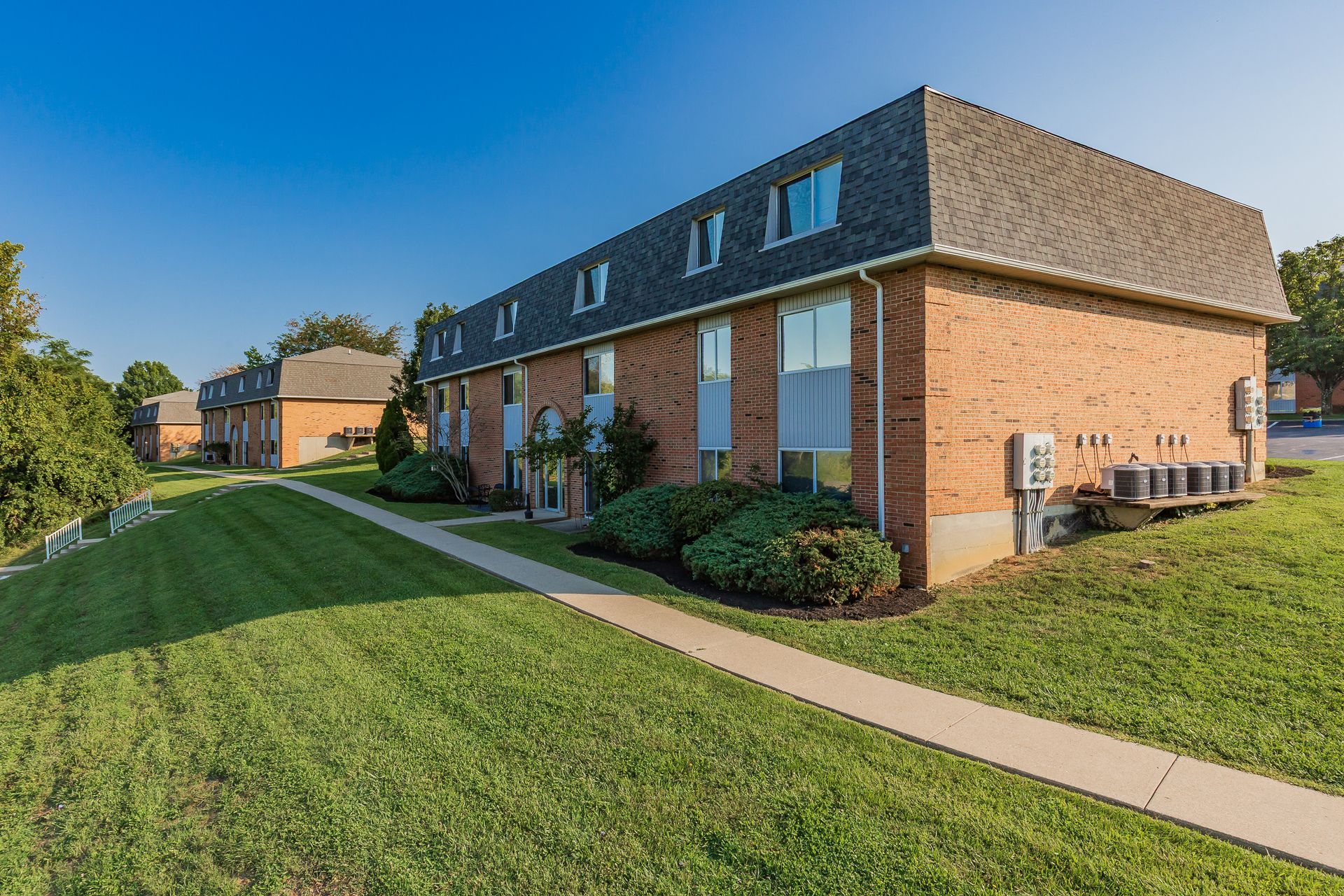 Brick apartment buildings beside a green lawn and sidewalk on a sunny day