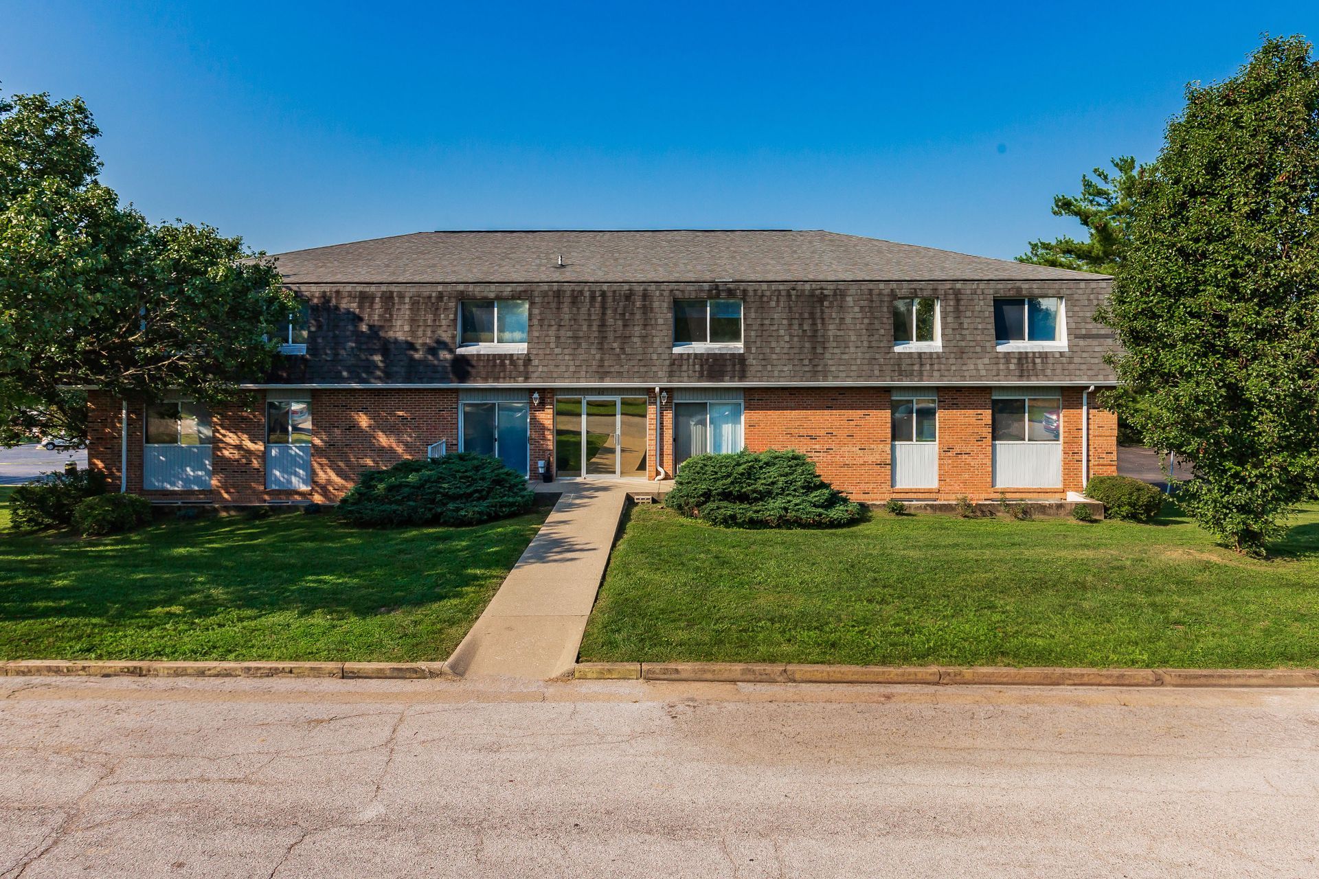 Two-story brick apartment building with a central walkway, green lawn, and blue sky