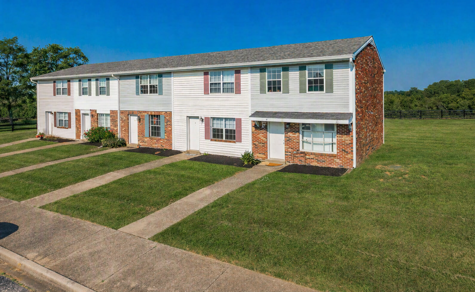 Row of white and brick townhouses with green lawns under a clear blue sky