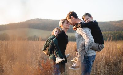 A man and woman face each other in a field,  carrying their children on their backs. 