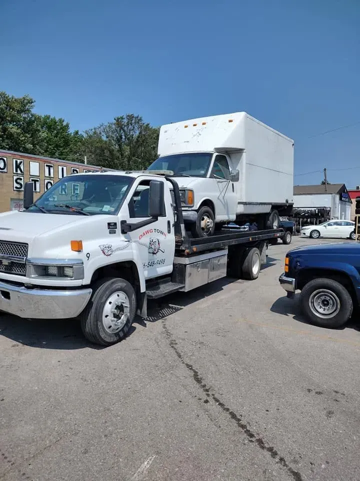 Tow truck carrying a white box truck in a parking lot on a sunny day