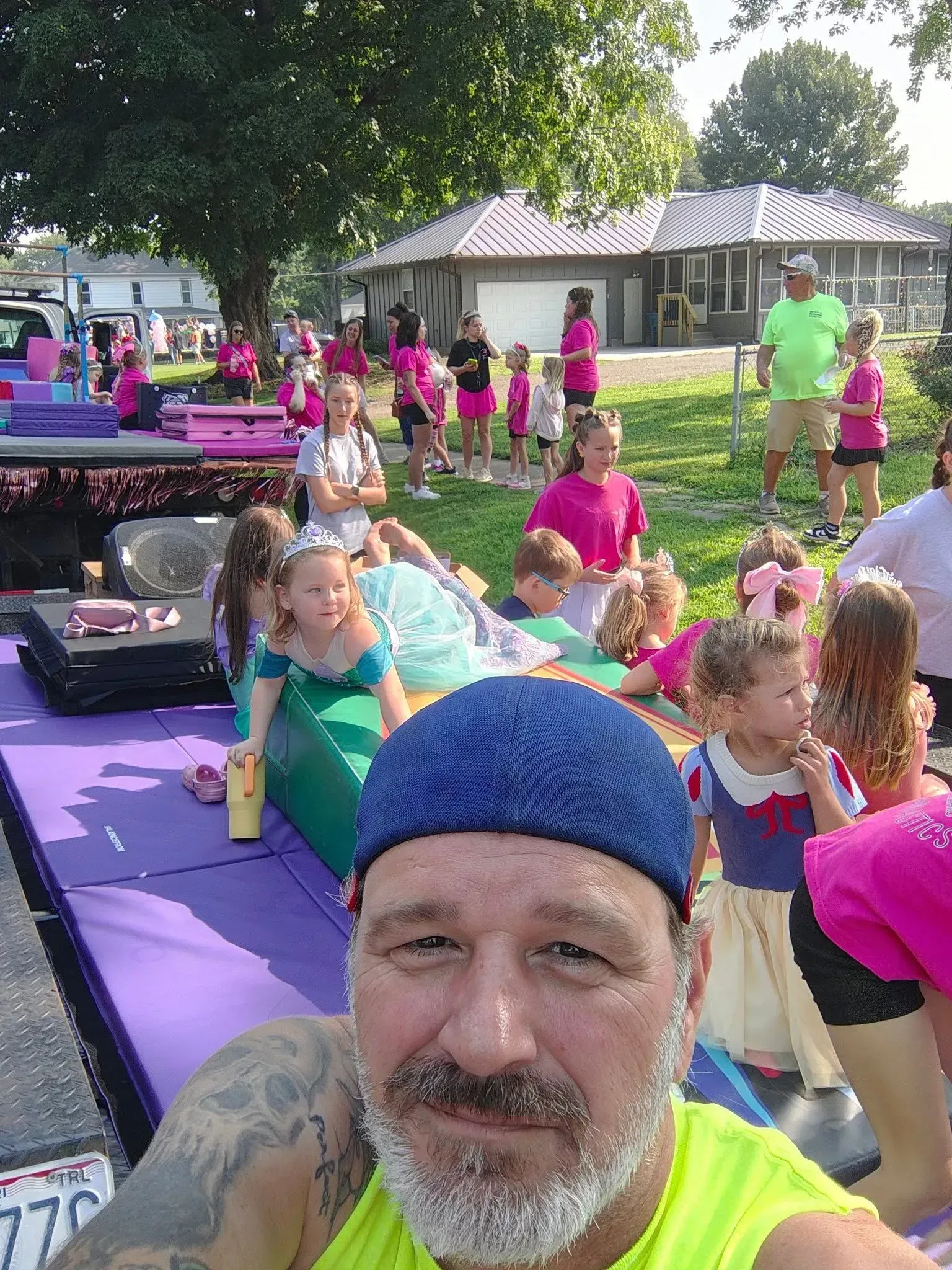 Selfie at a colorful outdoor fitness class with people on purple mats under a tree.