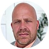 A bald man with a beard is wearing a suit and tie.