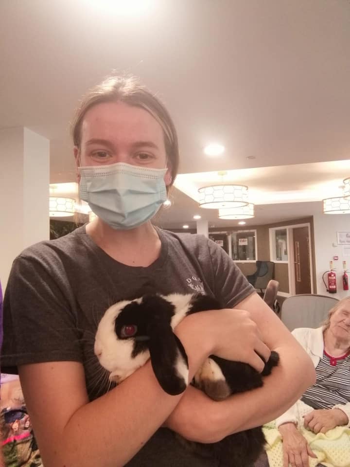 A woman wearing a mask is holding a black and white rabbit