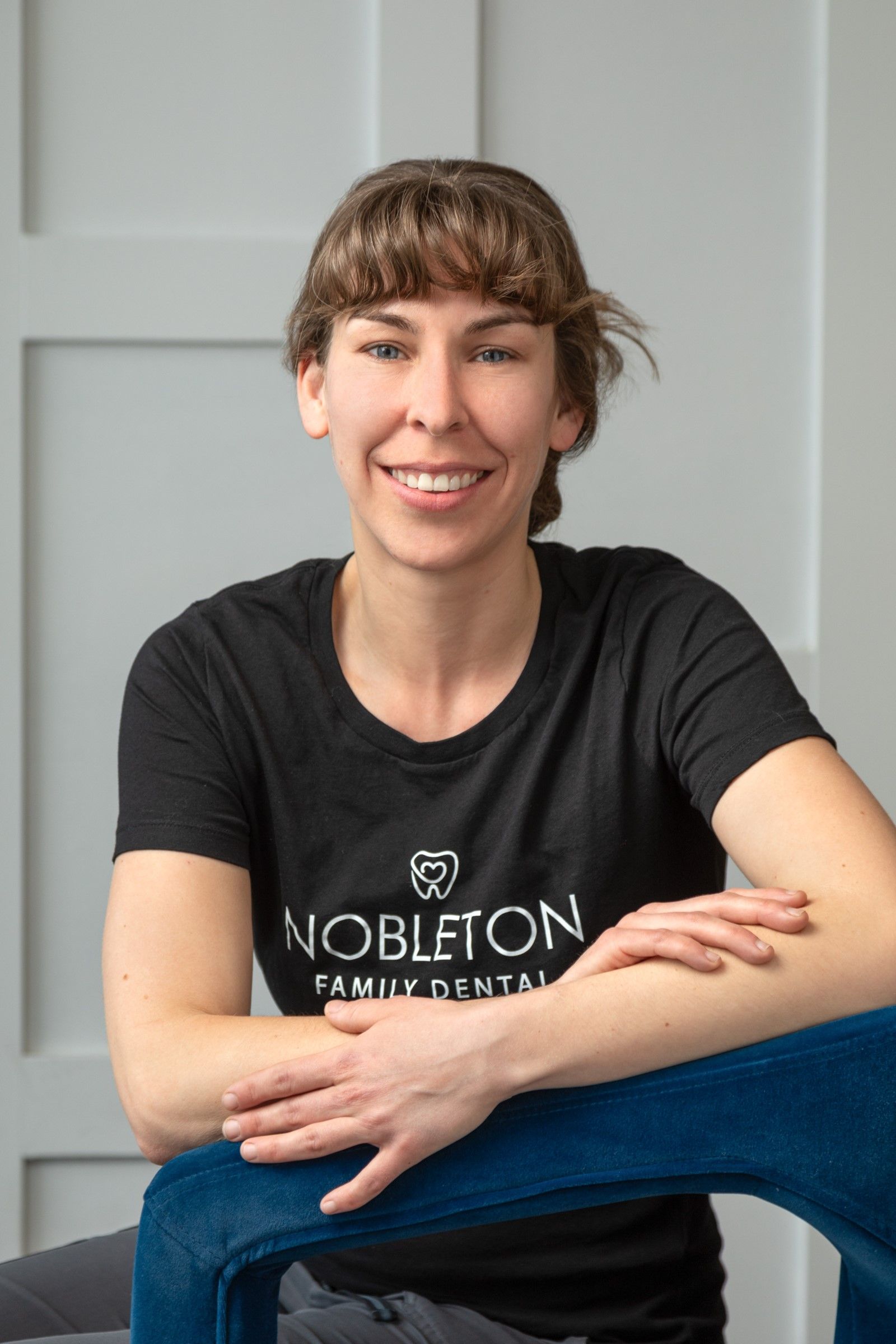 Woman wearing a black t-shirt, smiling, resting arms on a blue chair.