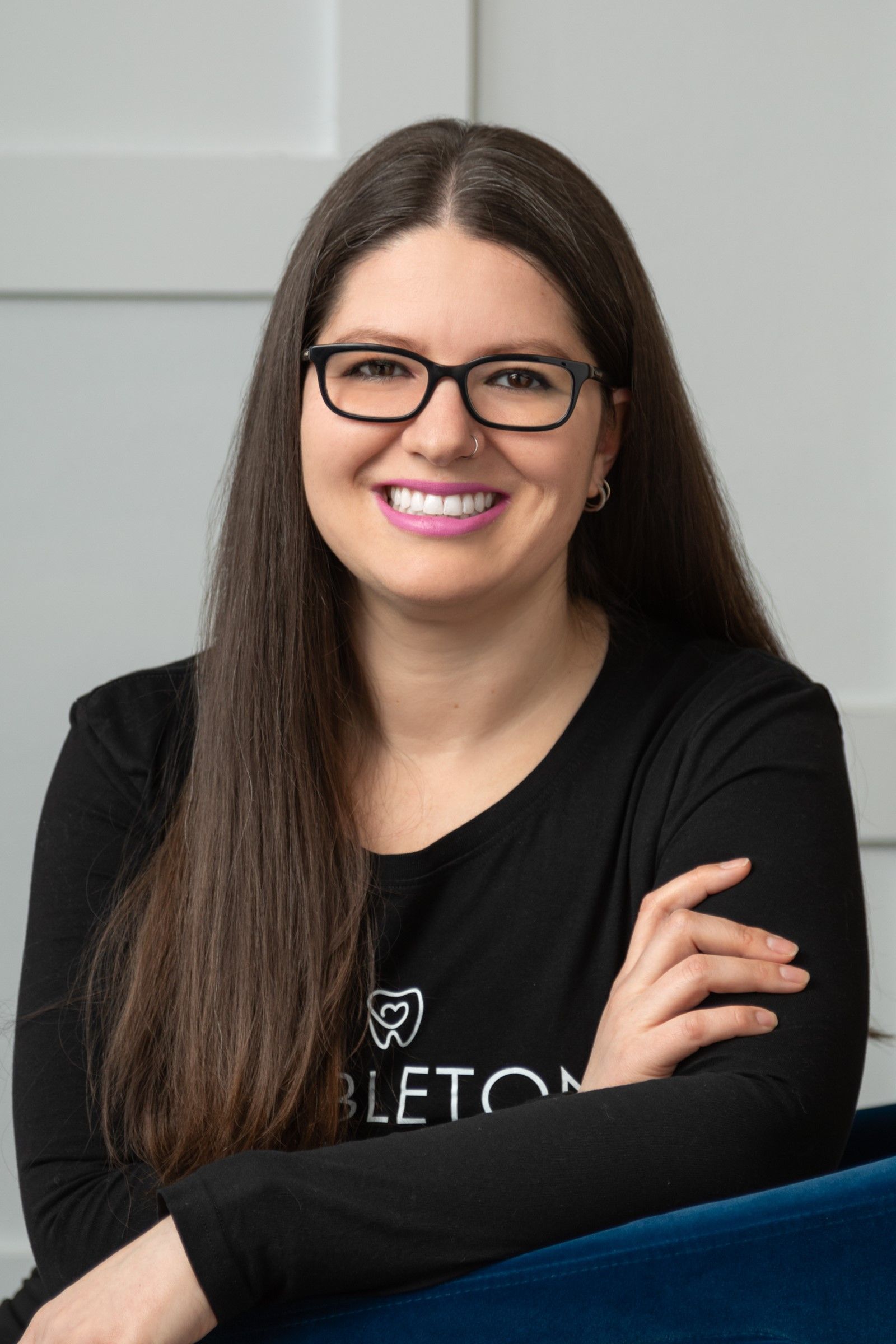 Woman with dark hair and glasses smiles with arms crossed, wearing a black shirt.