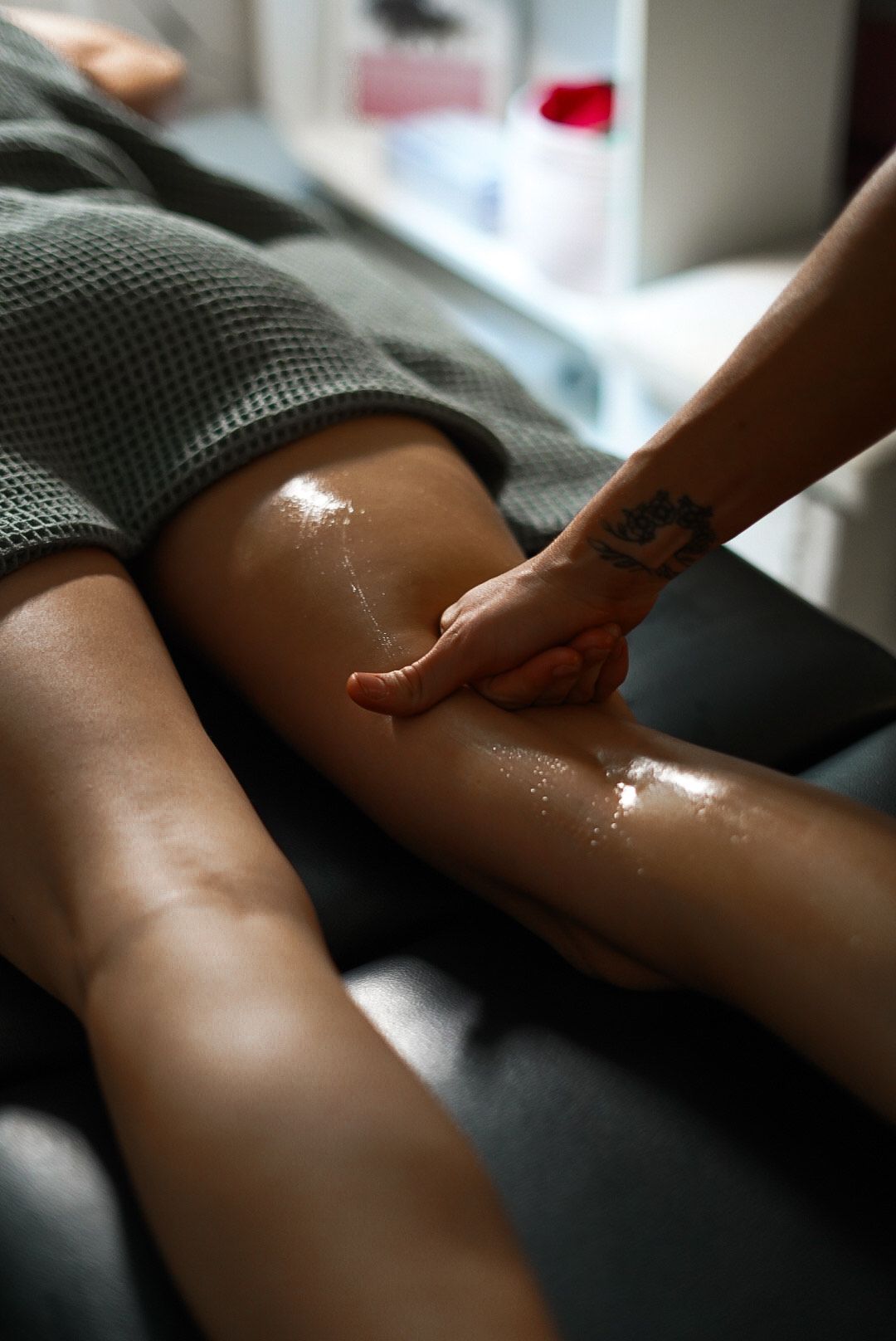 A leg being massaged with oil. A person's hand presses into the leg on a massage table.