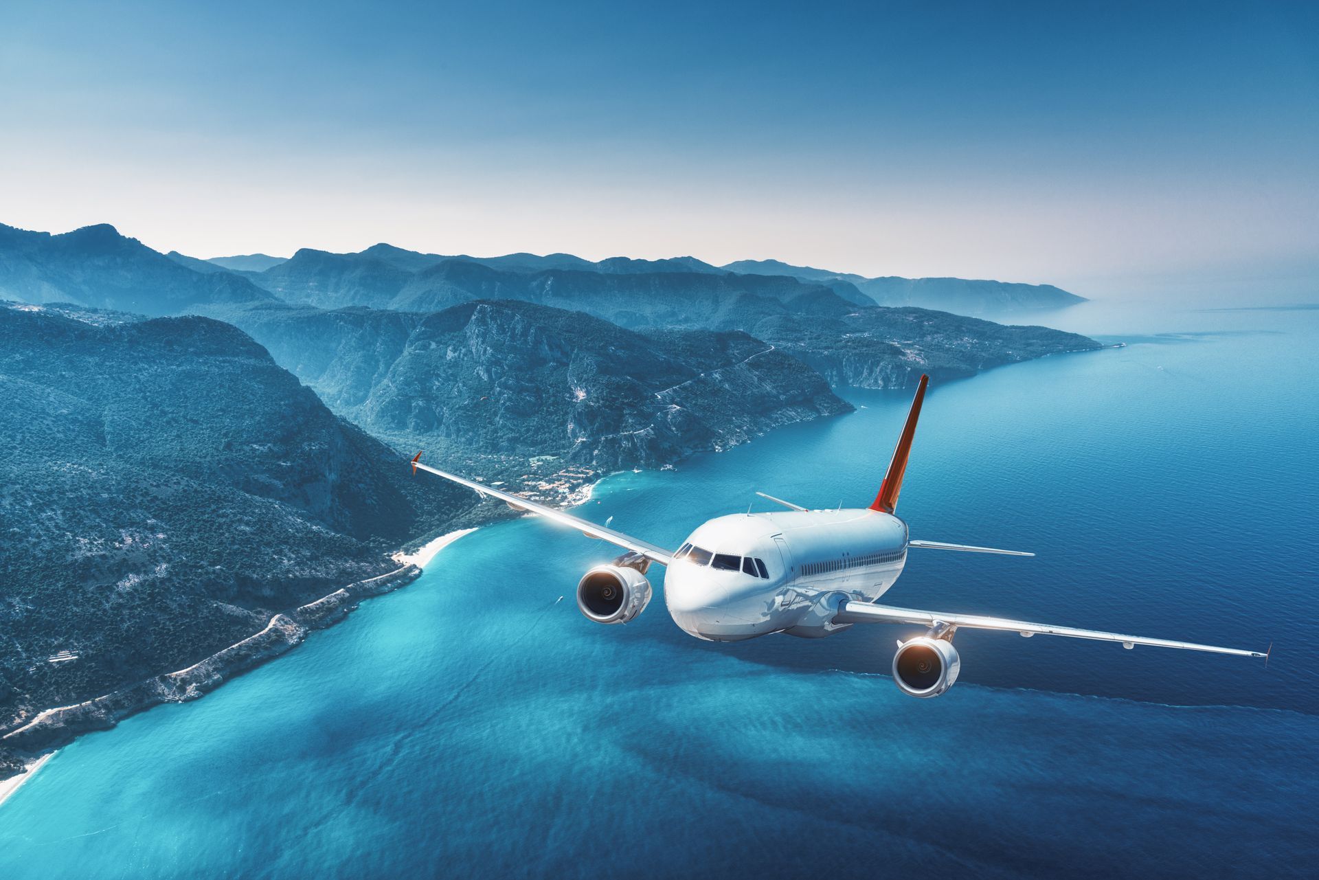 An airplane is flying over the ocean with mountains in the background.
