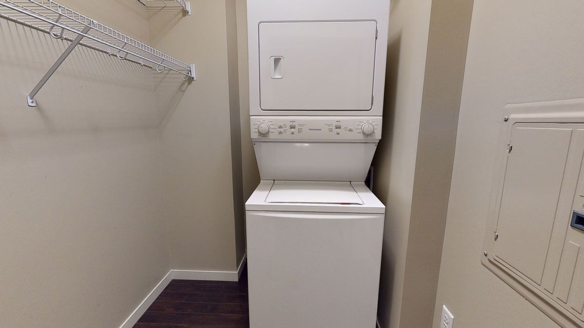 Laundry nook with stacked white washer and dryer in a small beige closet