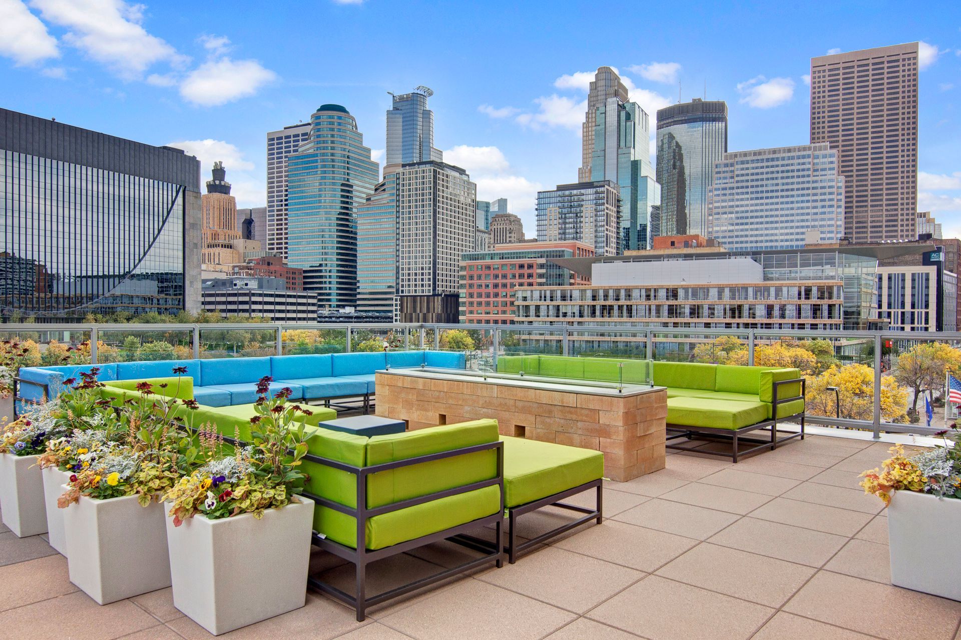 Rooftop lounge with green seating, planters, and city skyline under a clear blue sky