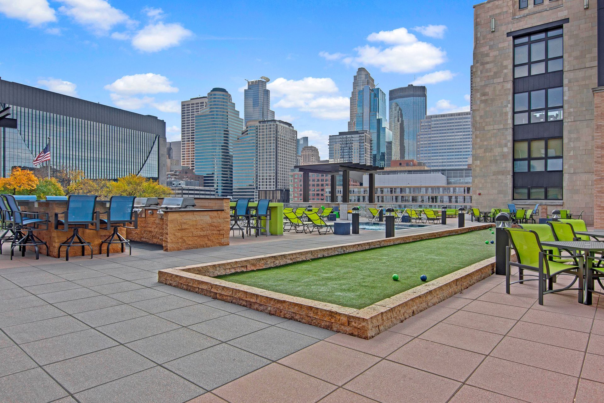 Rooftop patio with tables, green benches, and city skyline under a blue sky