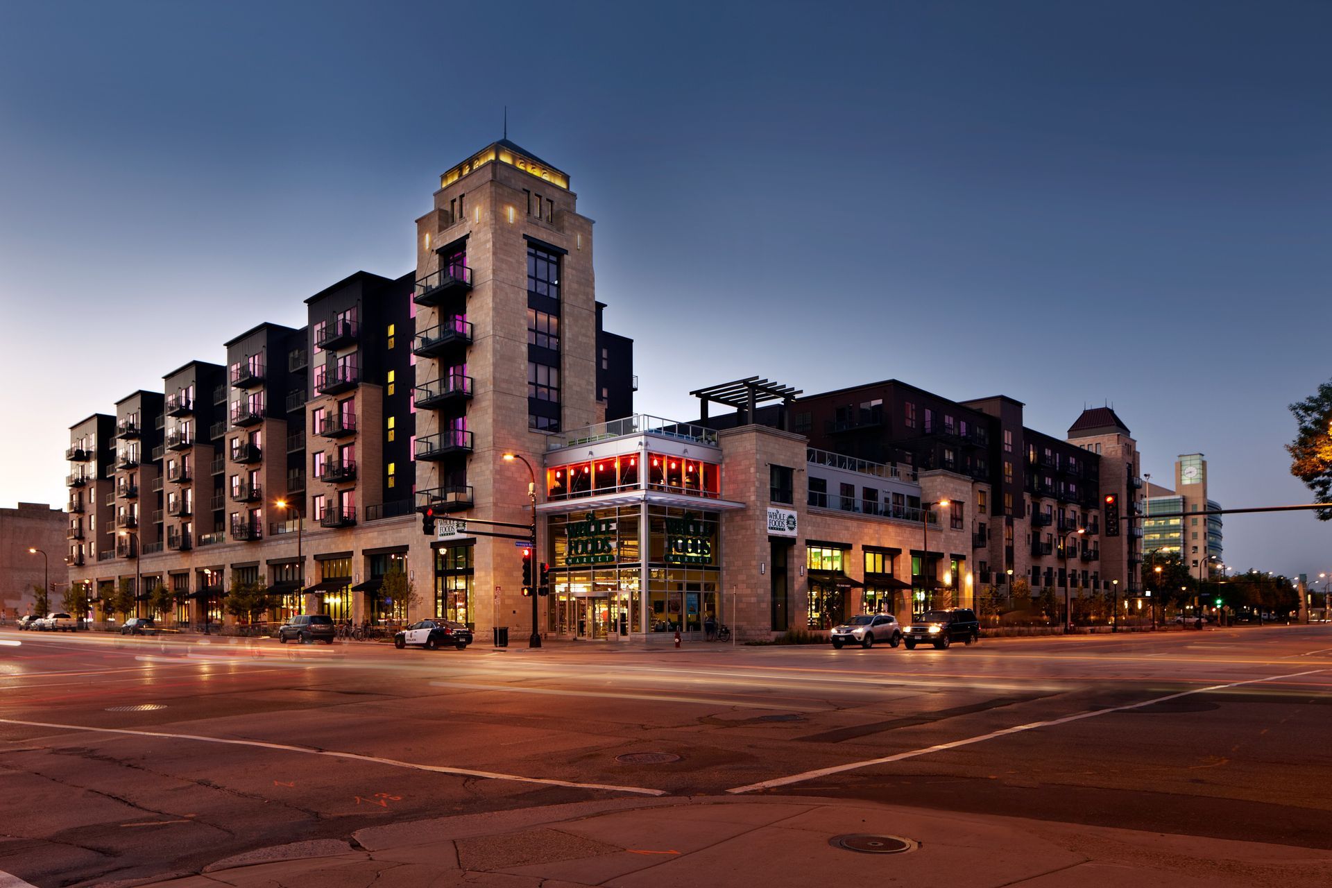 Modern apartment building at dusk on a city street corner, lit windows and streetlights visible