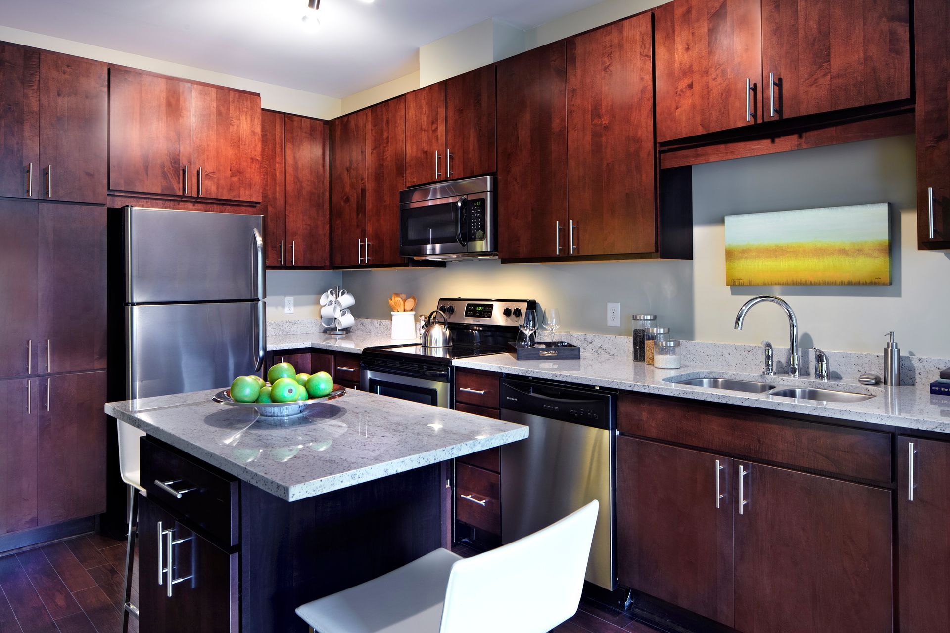 Modern kitchen with dark wood cabinets, stainless appliances, black countertops, and a central island with fruit bowl.