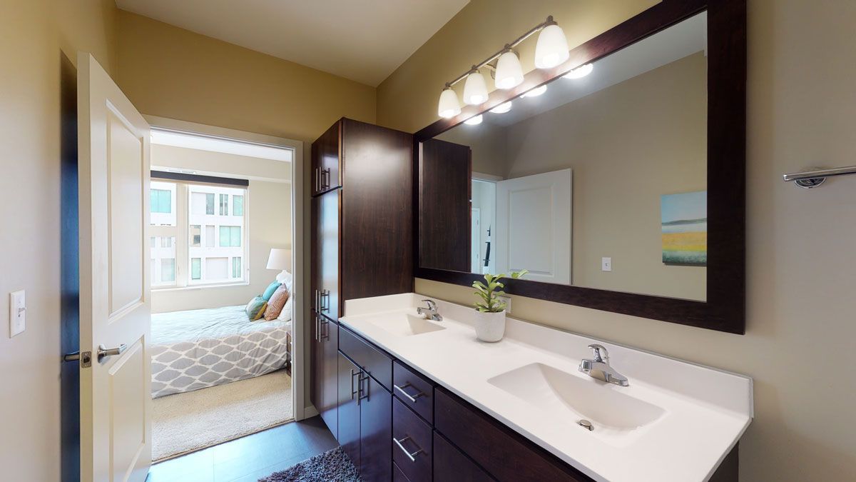 Bathroom vanity with large mirror and lights, viewed toward a bedroom through the open door.
