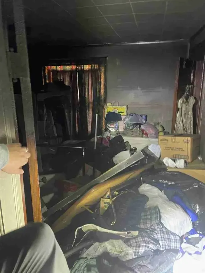 Cluttered, dim room with piled debris and hanging curtains; a hand and knee visible at left edge