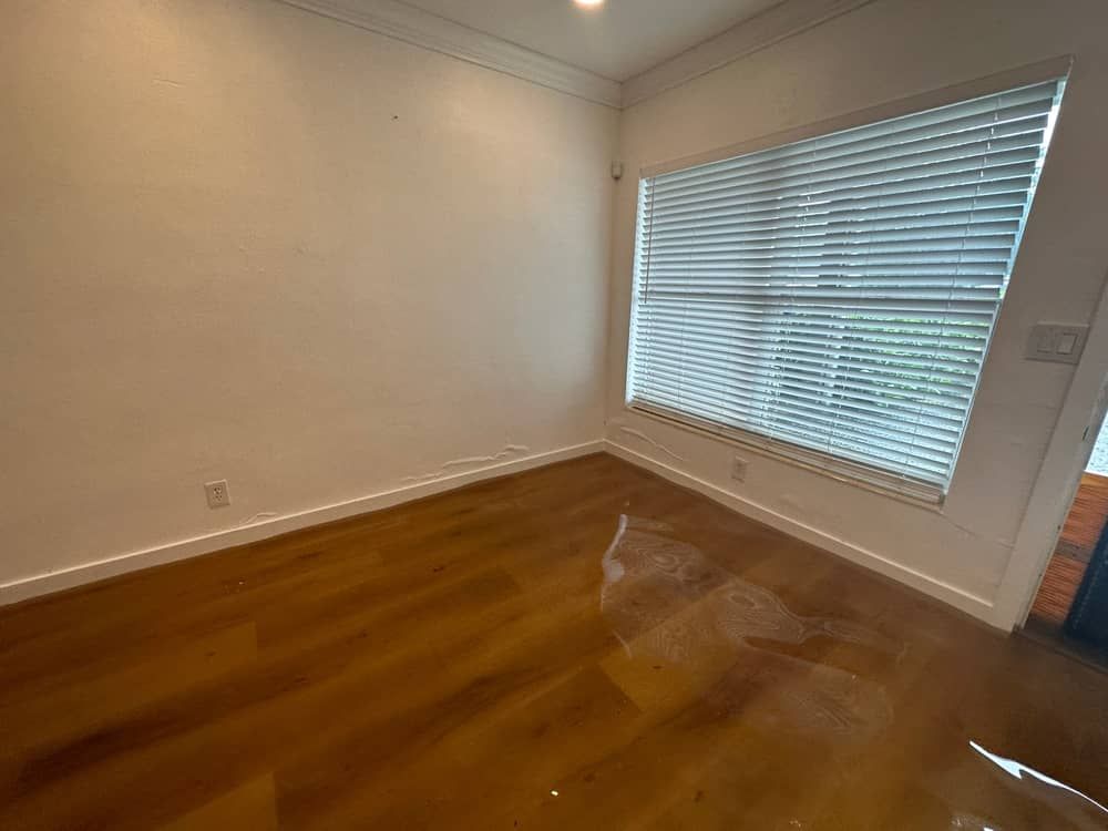 Empty room with hardwood floor, white walls, and a large window with blinds.