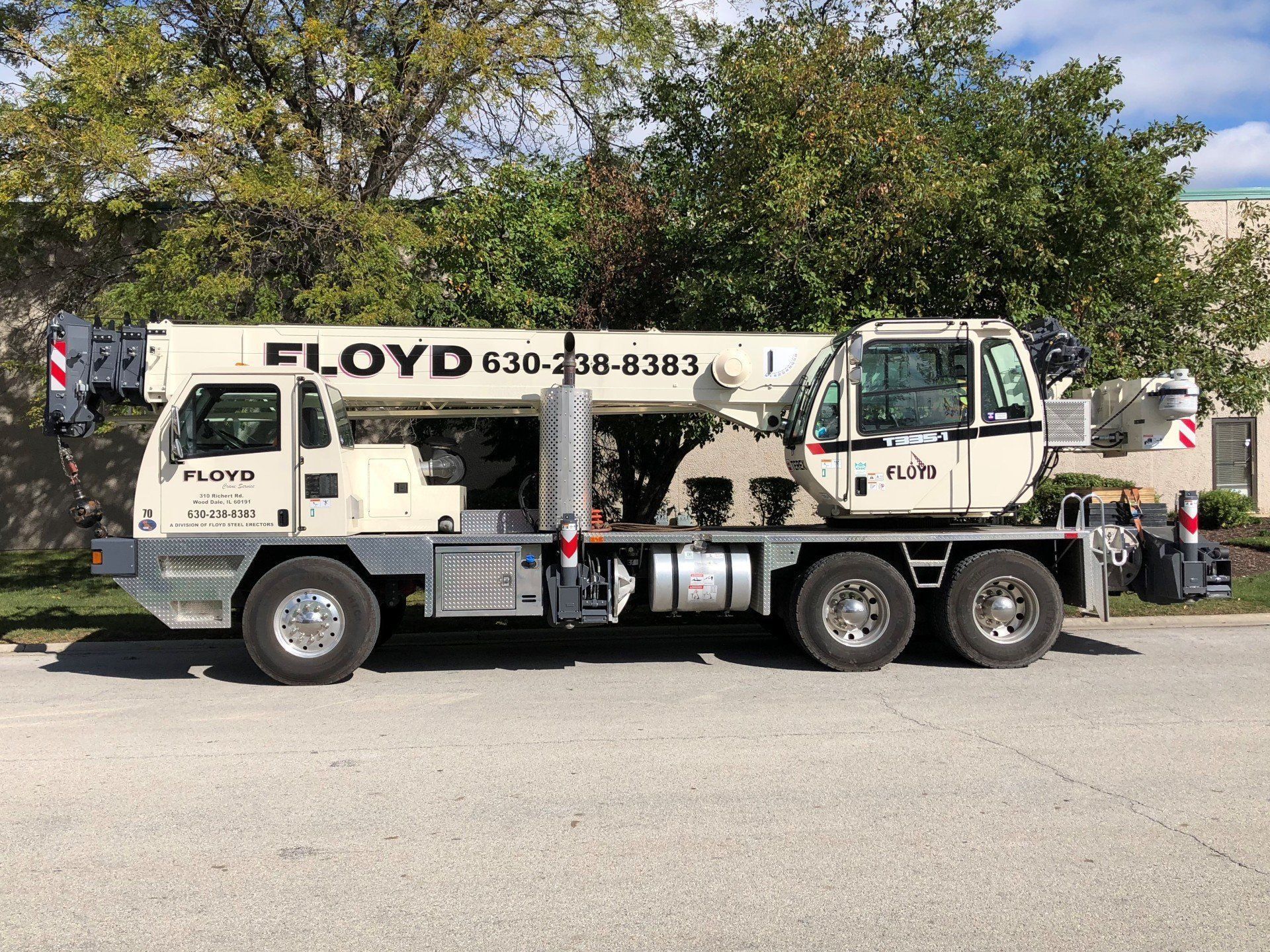 Tow truck with “FLOYD” logo parked on a street beside trees and a cloudy sky