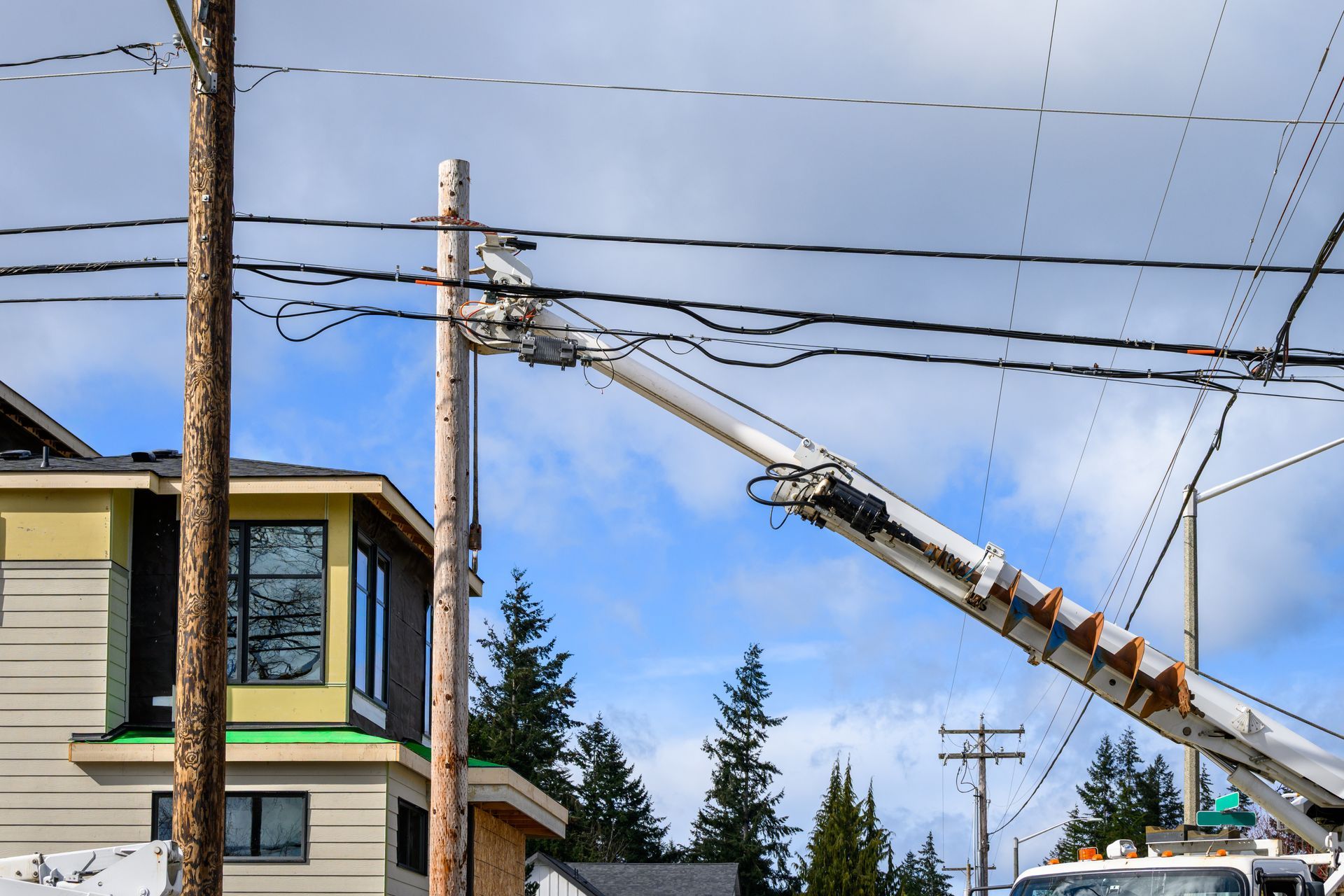 Utility truck lifting a worker near power lines beside a house on a residential street