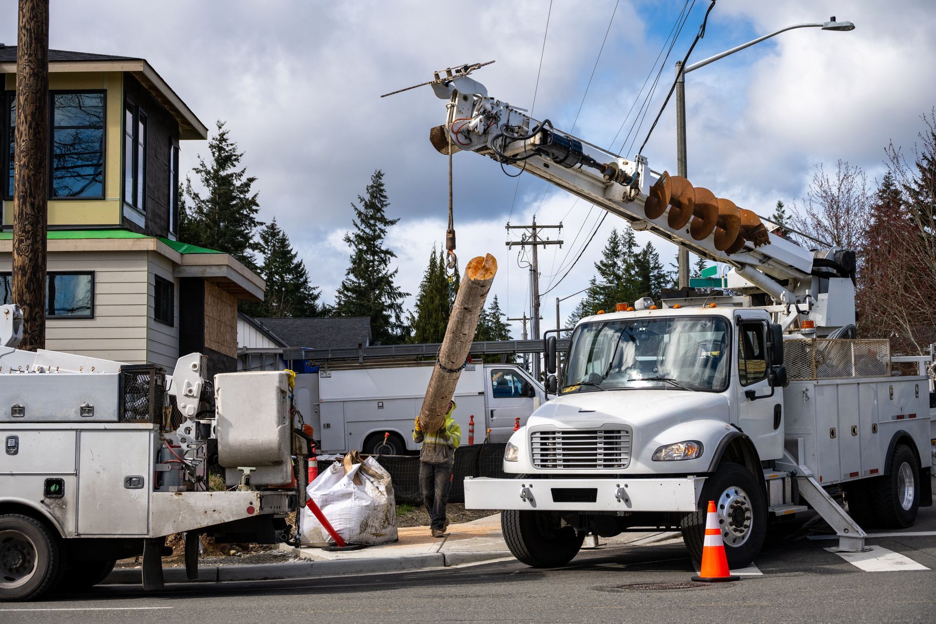 Utility truck with boom lift on a street beside a house, worker and traffic cone nearby Utility truck with boom lift on a street beside a house, worker and traffic cone nearby