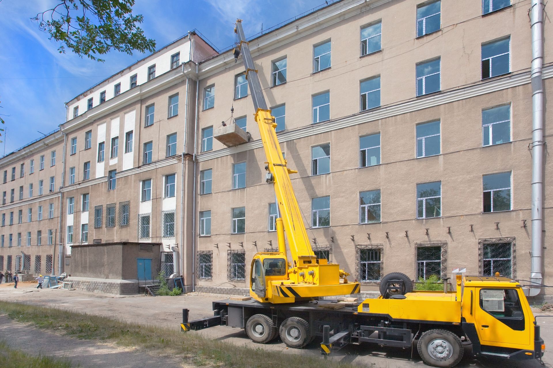 Yellow crane truck lifting materials beside a beige apartment building under construction Yellow crane truck lifting materials beside a beige apartment building under construction